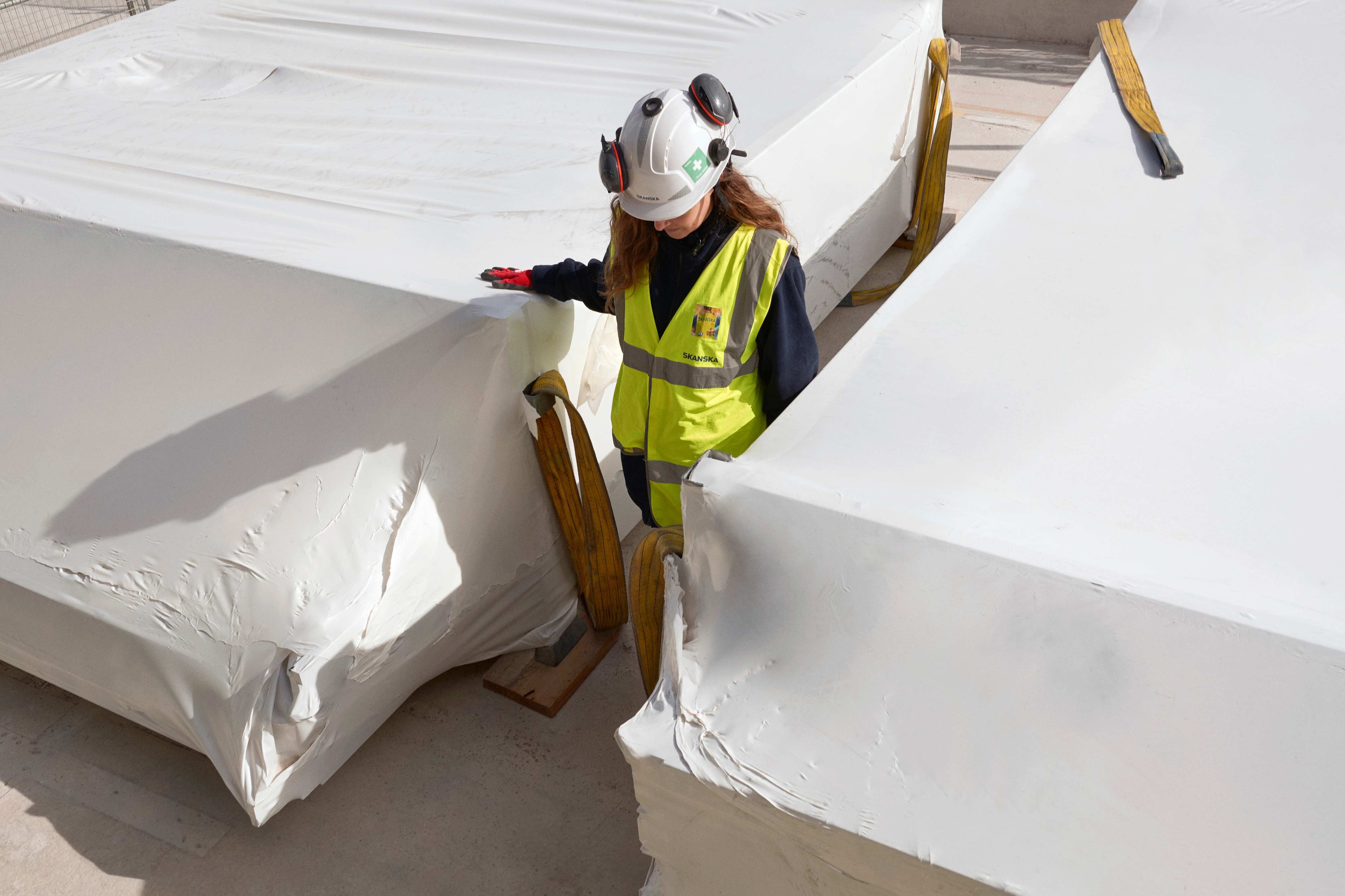En arbetare i skyddsutrustning inspekterar stora, inslagna industriella material utomhus.