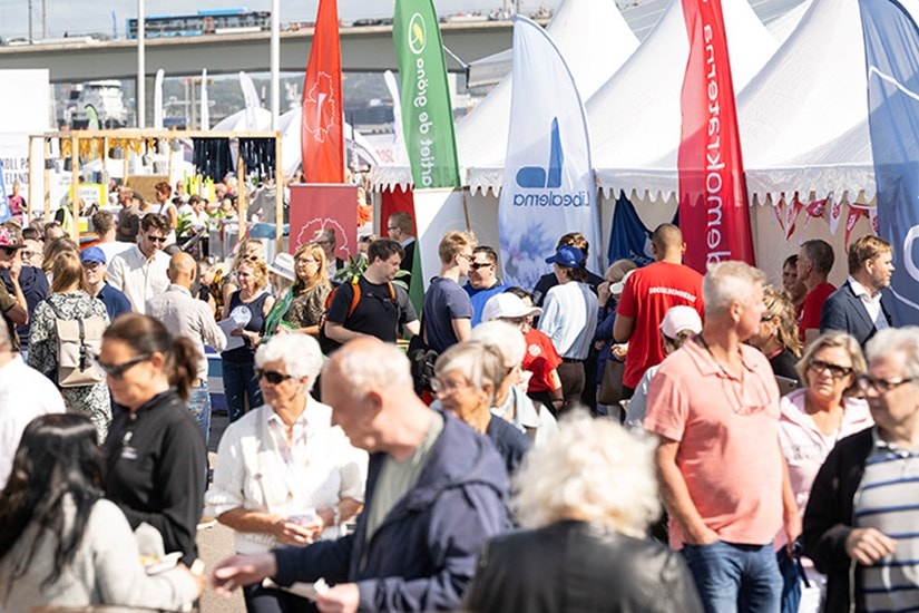 Folkmassa vid en utomhusmarknad eller festival med färgglada tält och banderoller.