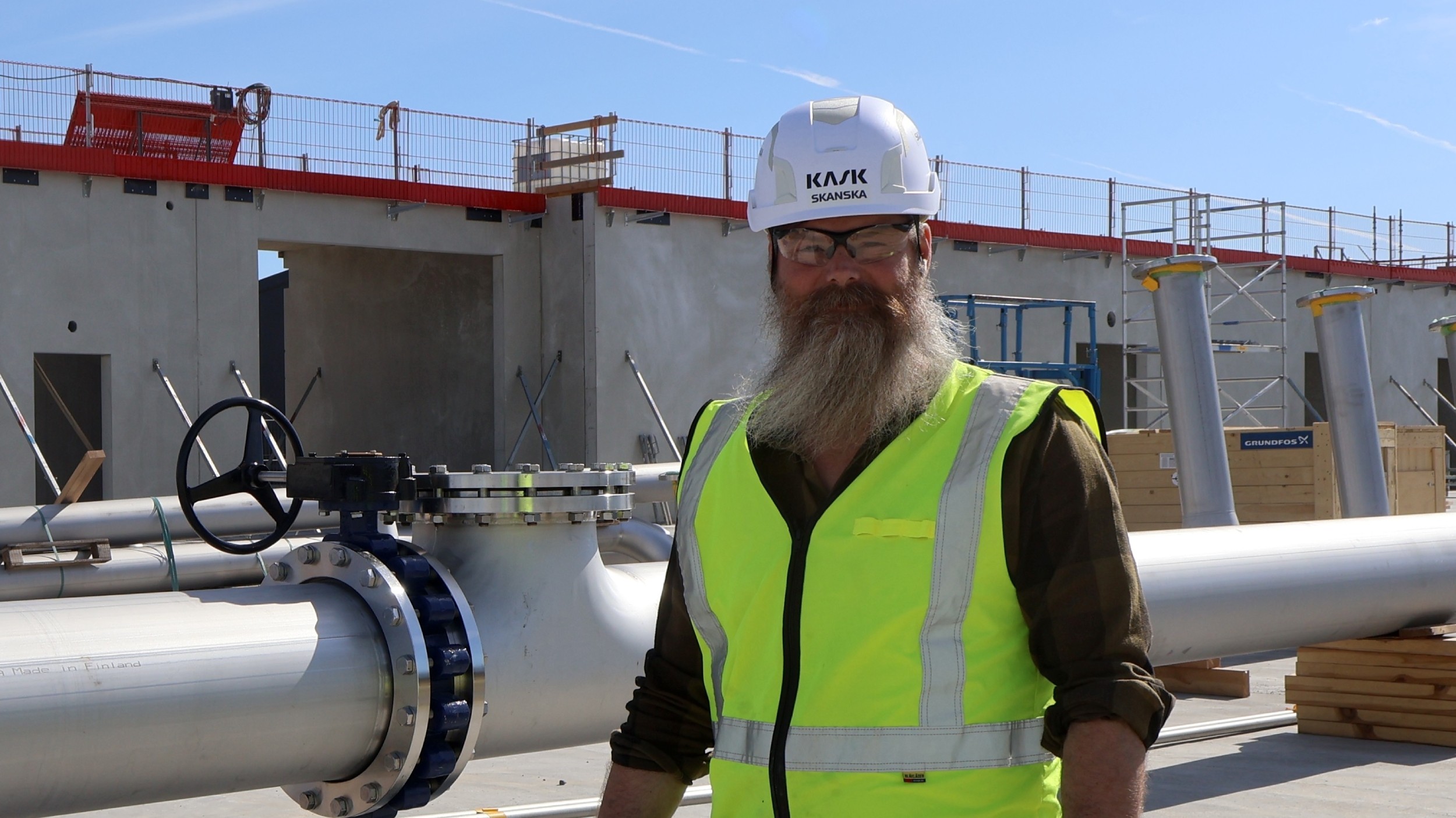 Skanskamedarbetare i hjälm och skyddsutrustning står ute på ett byggprojekt.