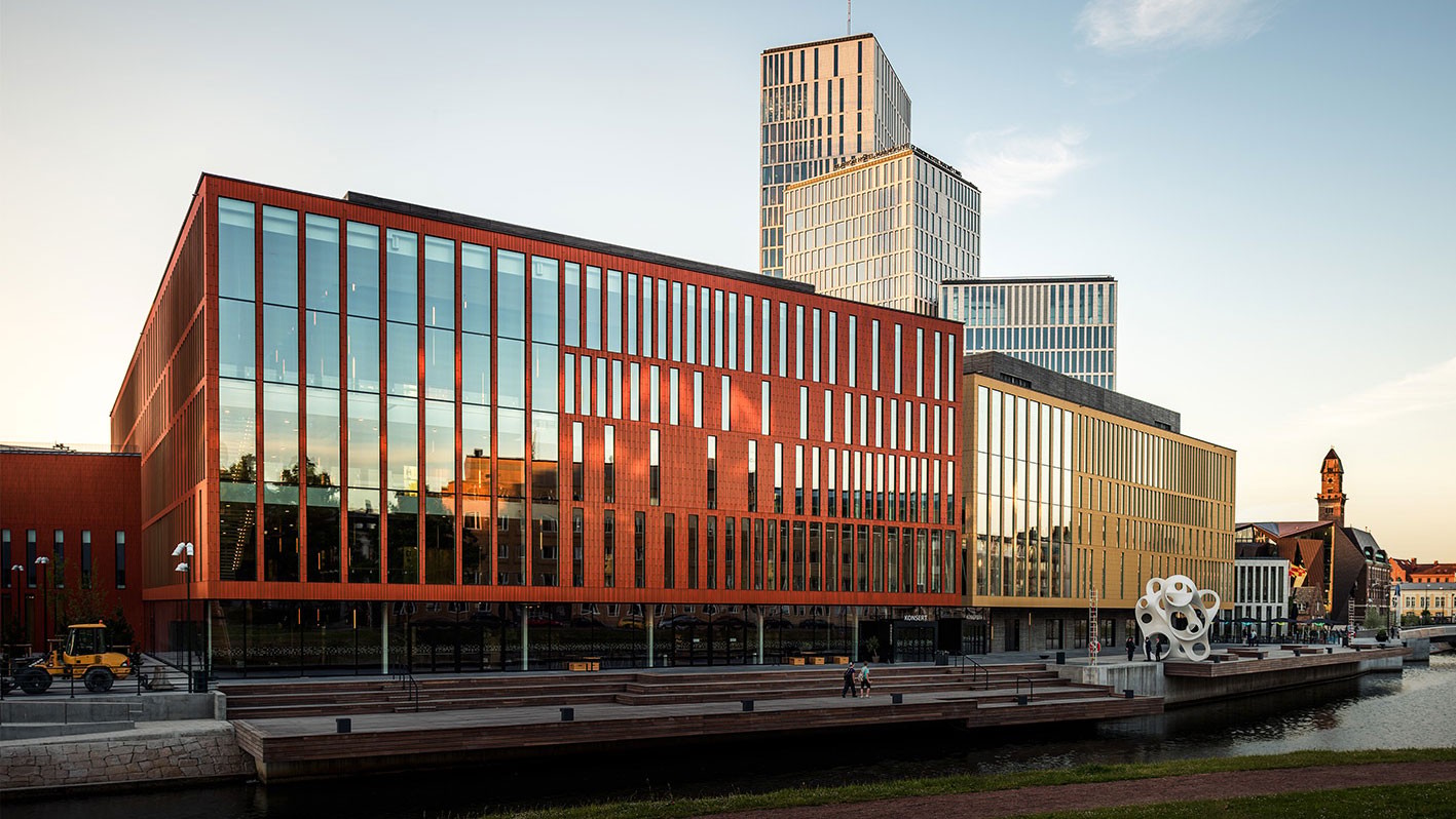 Moderna byggnader med stora glasfönster vid en vattenfront under en klar himmel.