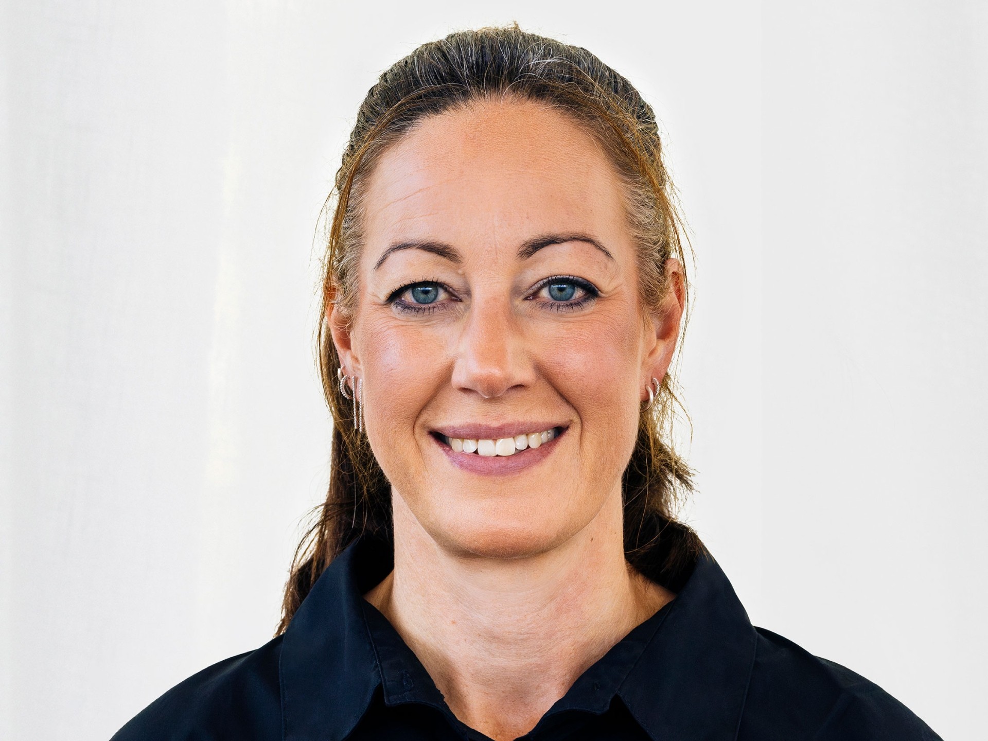 En person med långt hår som bär en mörk skjorta med krage mot en enkel vit bakgrund.