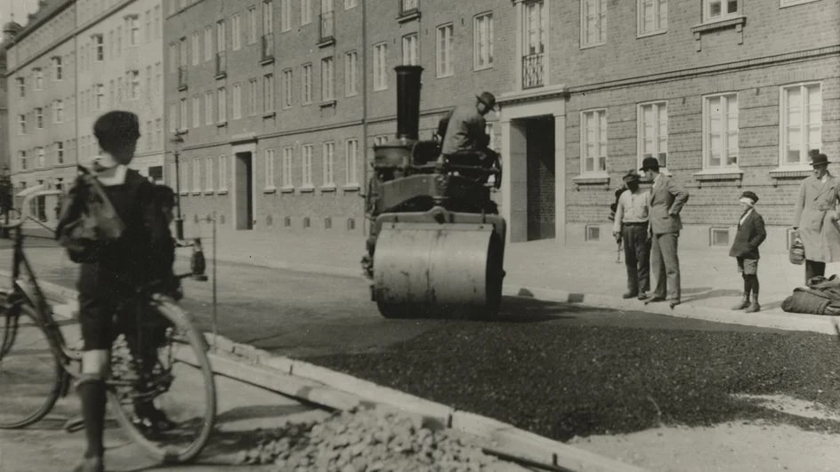 Vintage svartvit bild på arbetare som asfalterar en stadsgata med en ångvält.