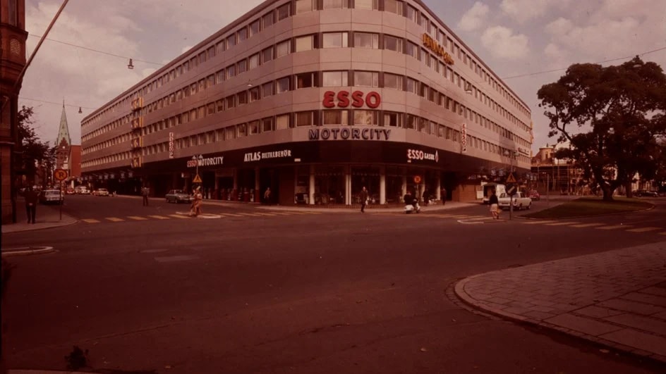 Stort hörnhus med Esso- och Motorcity-skyltar vid en lugn stadsgatkorsning.