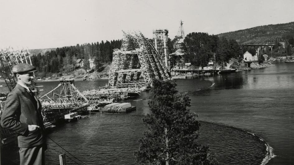Svartvit foto av en stor bågbro över en delvis frusen flod med kullar.
