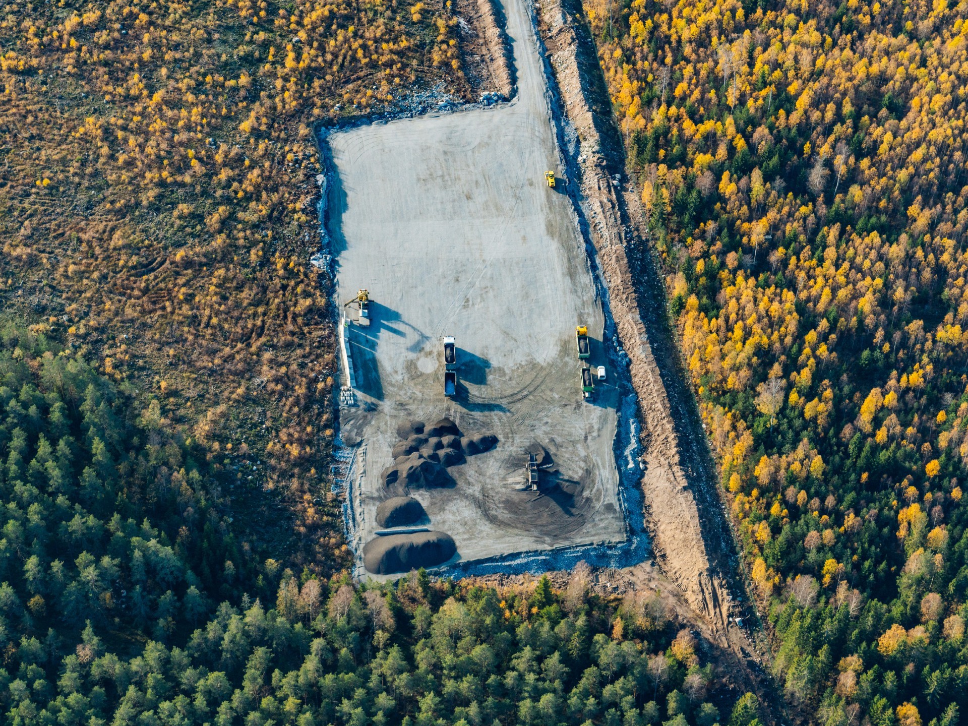 Flygfoto av en byggarbetsplats omgiven av tät höstskog med maskiner.
