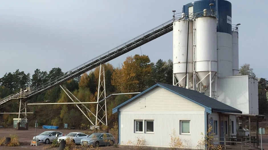 Industrial cement plant with storage silos and conveyor belt Industriell cementfabrik med silos, transportband och parkerade bilar i höstmiljö.