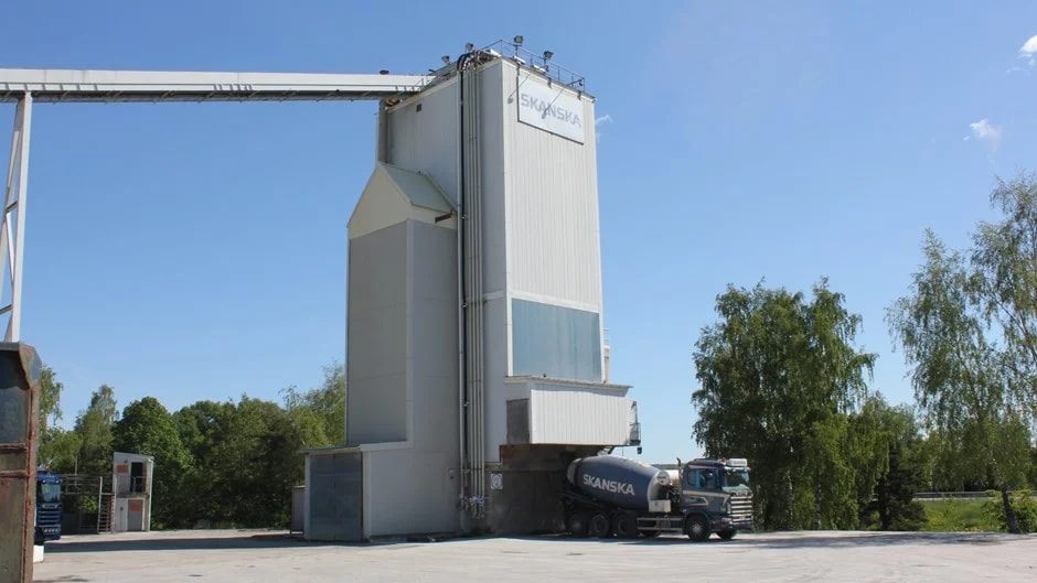 Modern Skanska Cement Plant with Truck in Clear Weather Betongblandningsanläggning med Skanska-lastbil under klarblå himmel och gröna träd.