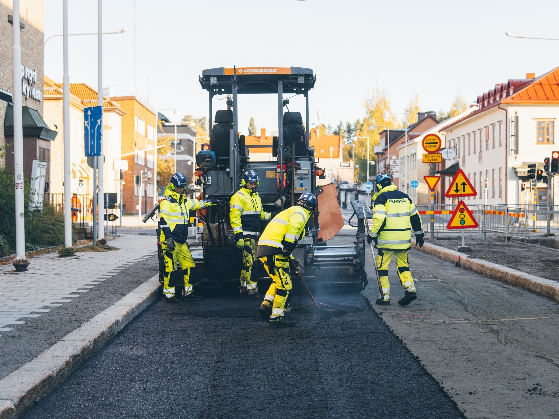Vägarbetare i skyddsutrustning som använder asfaltläggningsmaskin på stadsgata.