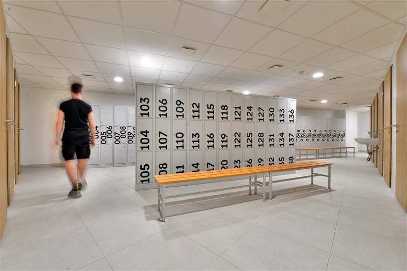 Modern locker room with numbered lockers, benches, and a person walking, featuring a clean design.