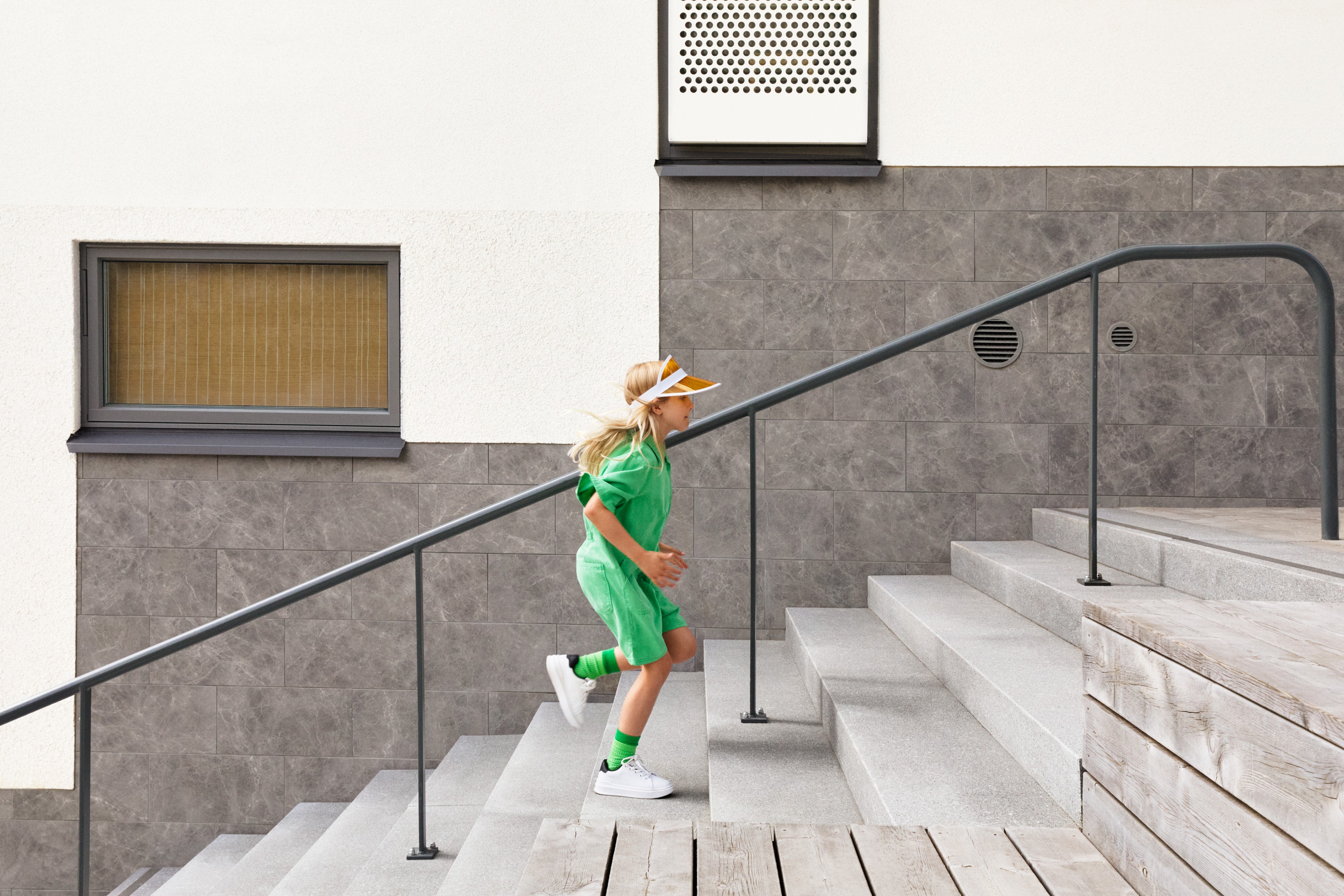 Responsibly managing for the future Child in green outfit running up outdoor concrete stairs with modern building background.