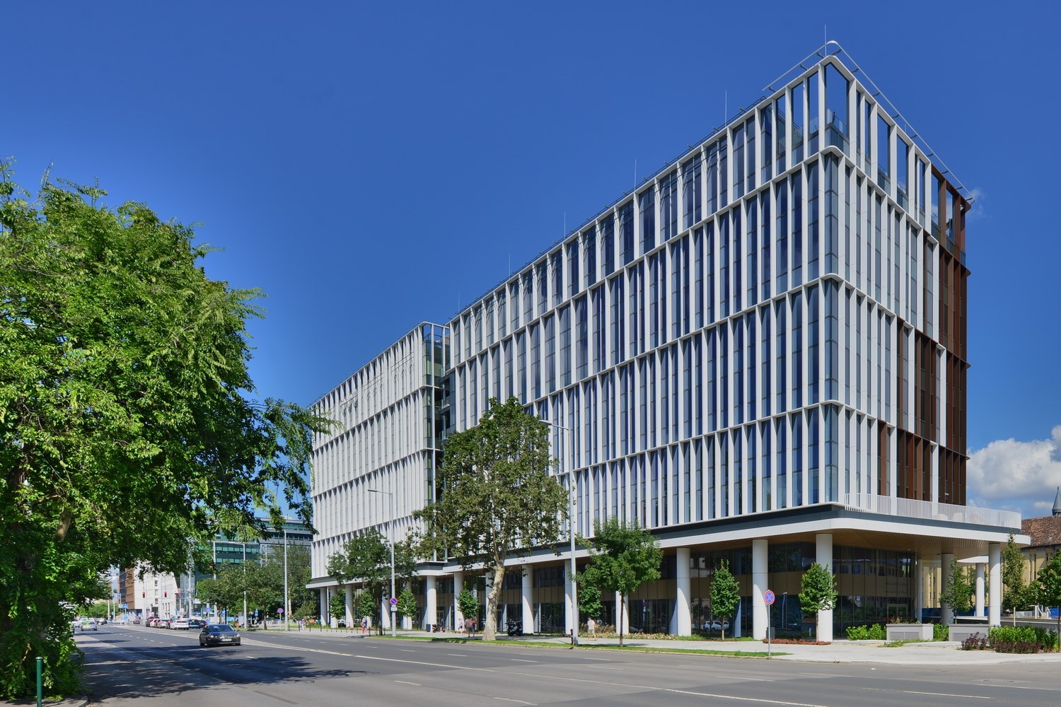Modern multi-story office building with glass facade and street view under a clear blue sky.