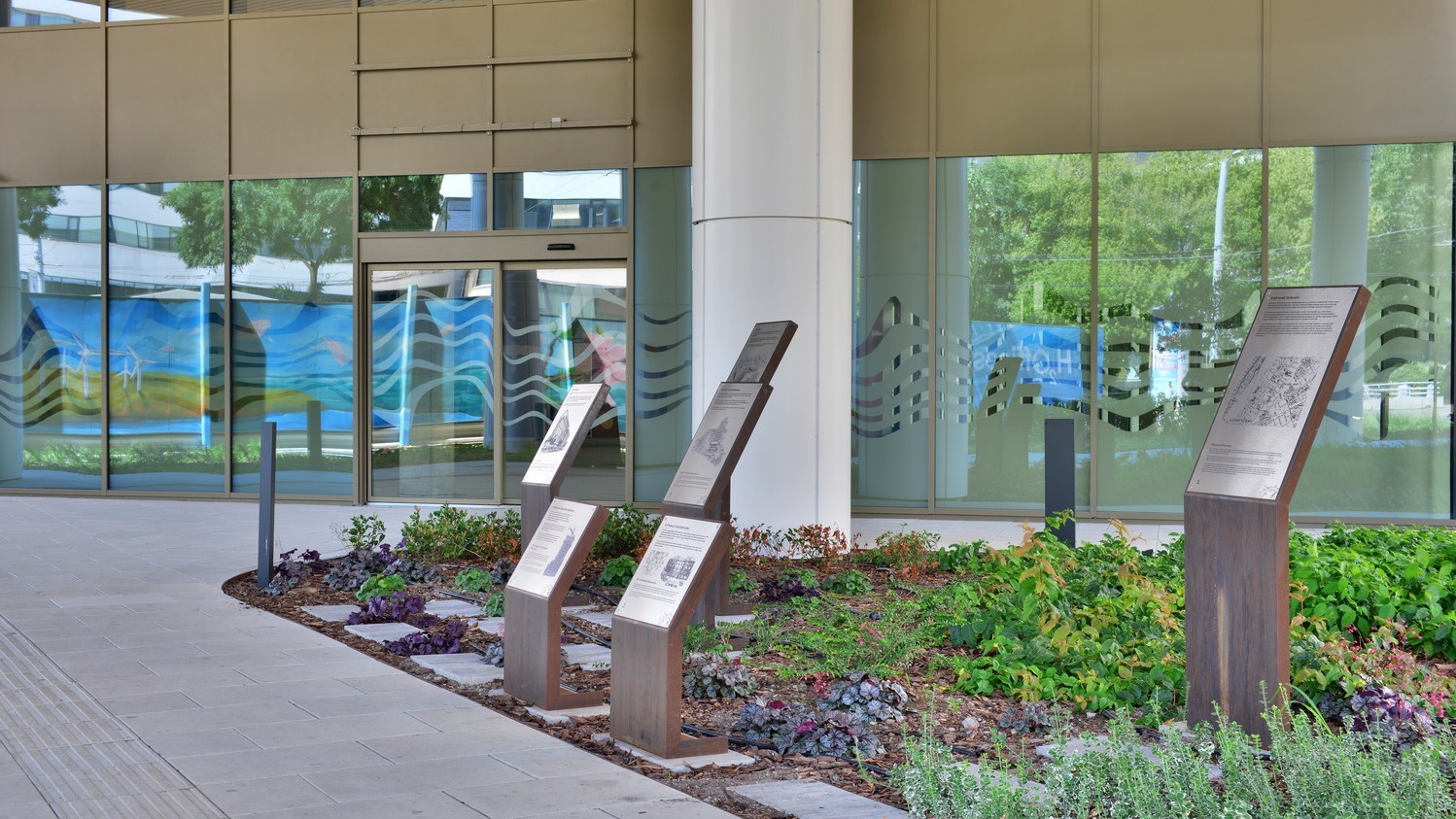 Modern building exterior with reflective glass, stone-edged pond, and lush greenery in urban setting.