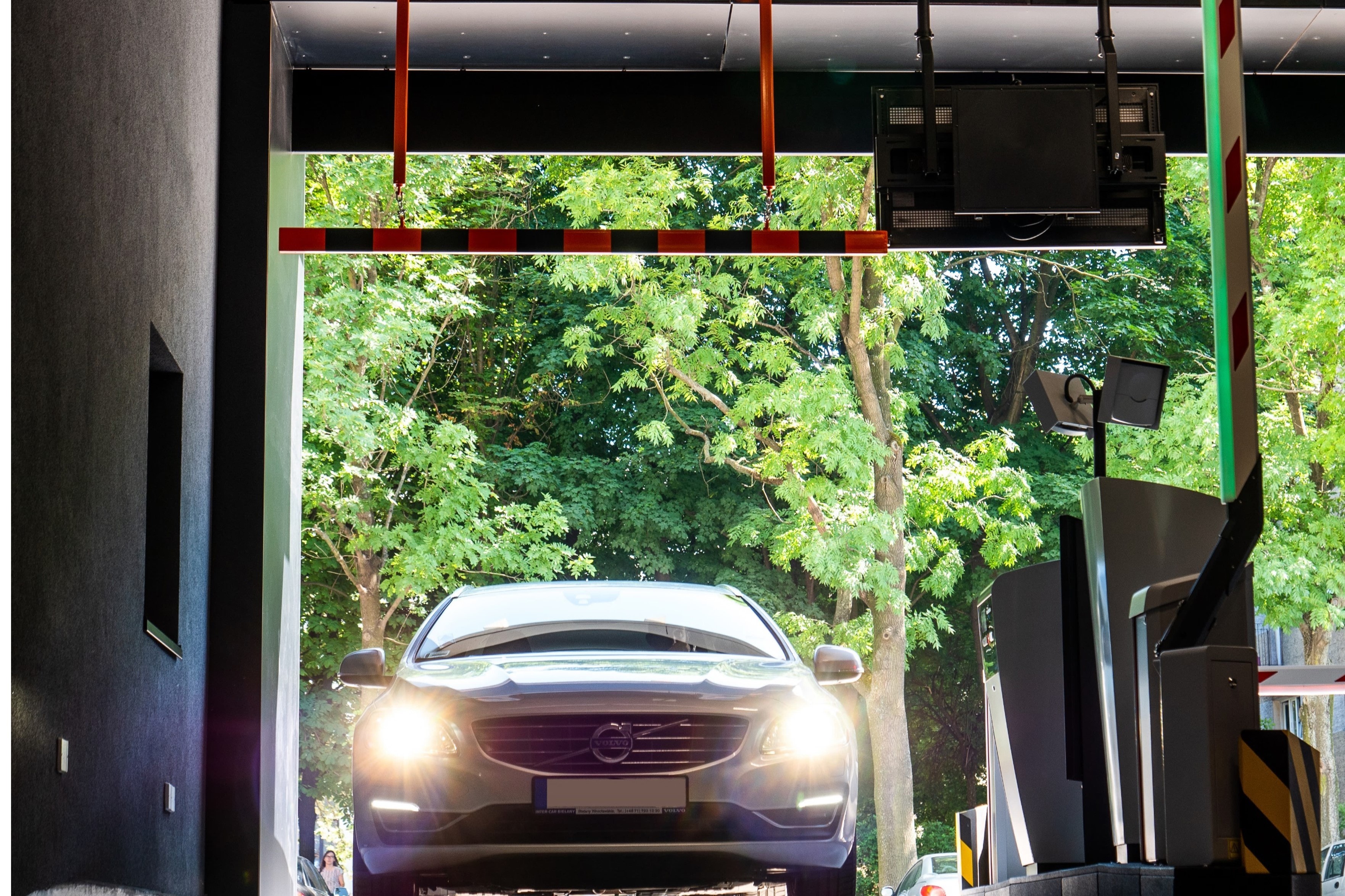 Car entering parking garage with headlights on, passing under a red and white barrier.