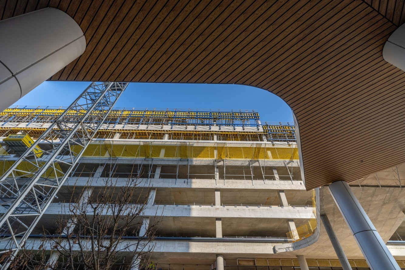 Modern concrete building under construction with scaffolding and clear blue sky.
