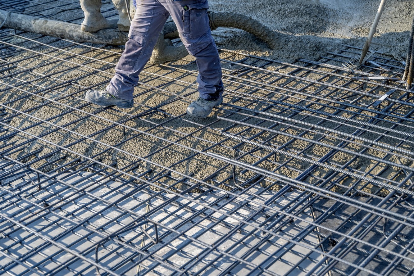 Construction workers pouring concrete over steel rebar for building foundation.