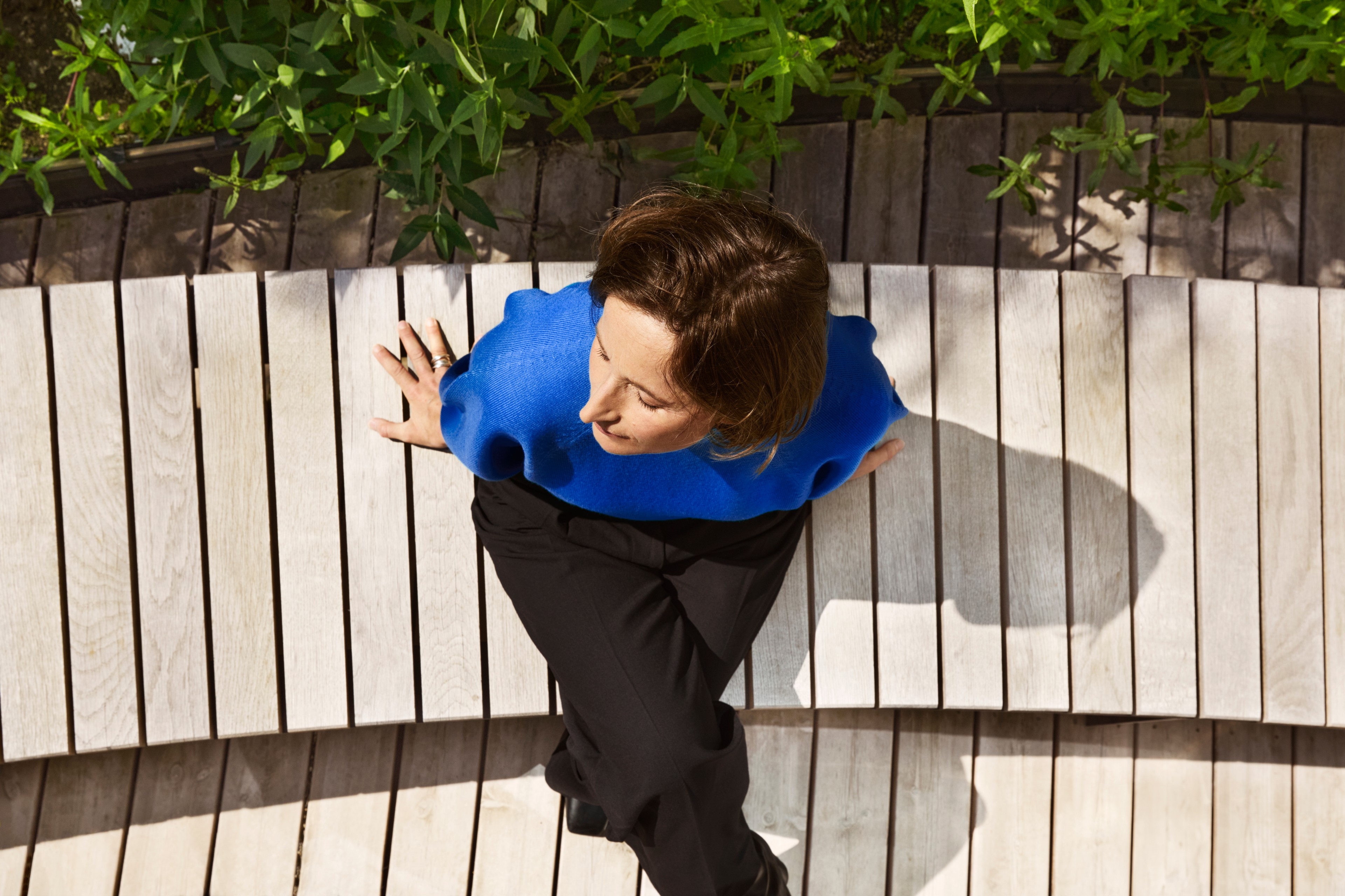Top view of a person in a blue sweater sitting on curved wooden steps outdoors.