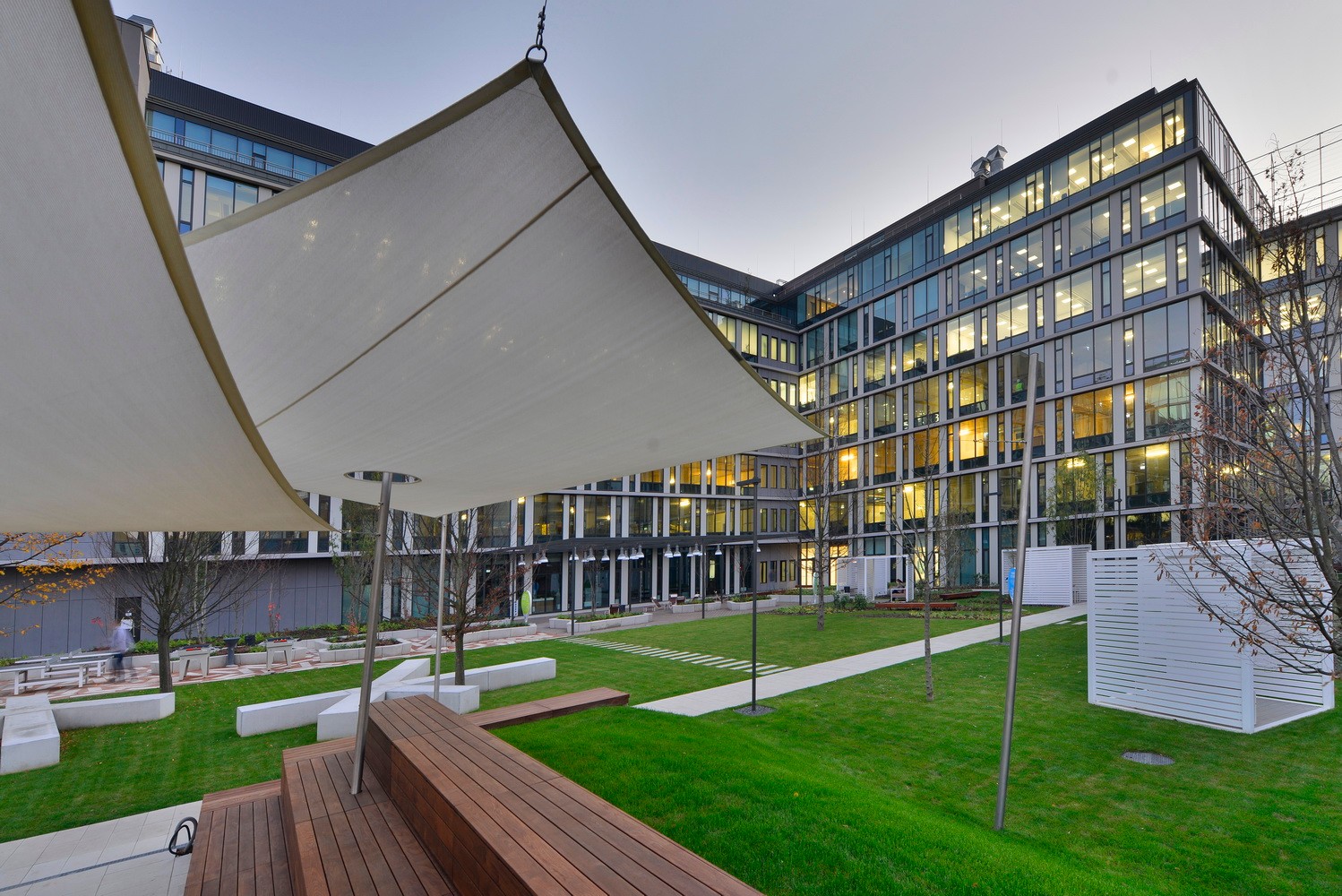 Modern office building with large windows, surrounded by landscaped green space and seating areas.
