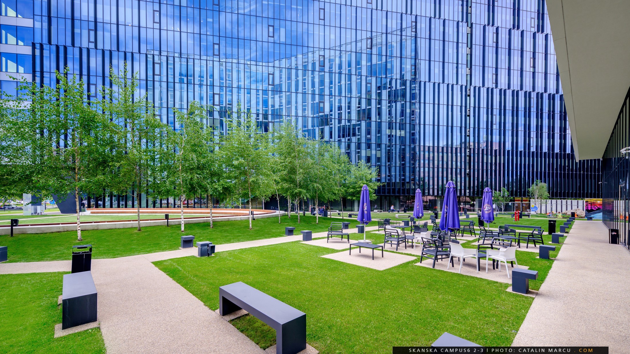 Campus 6 placemakig Modern office building with glass facade, surrounded by green space and outdoor seating area.