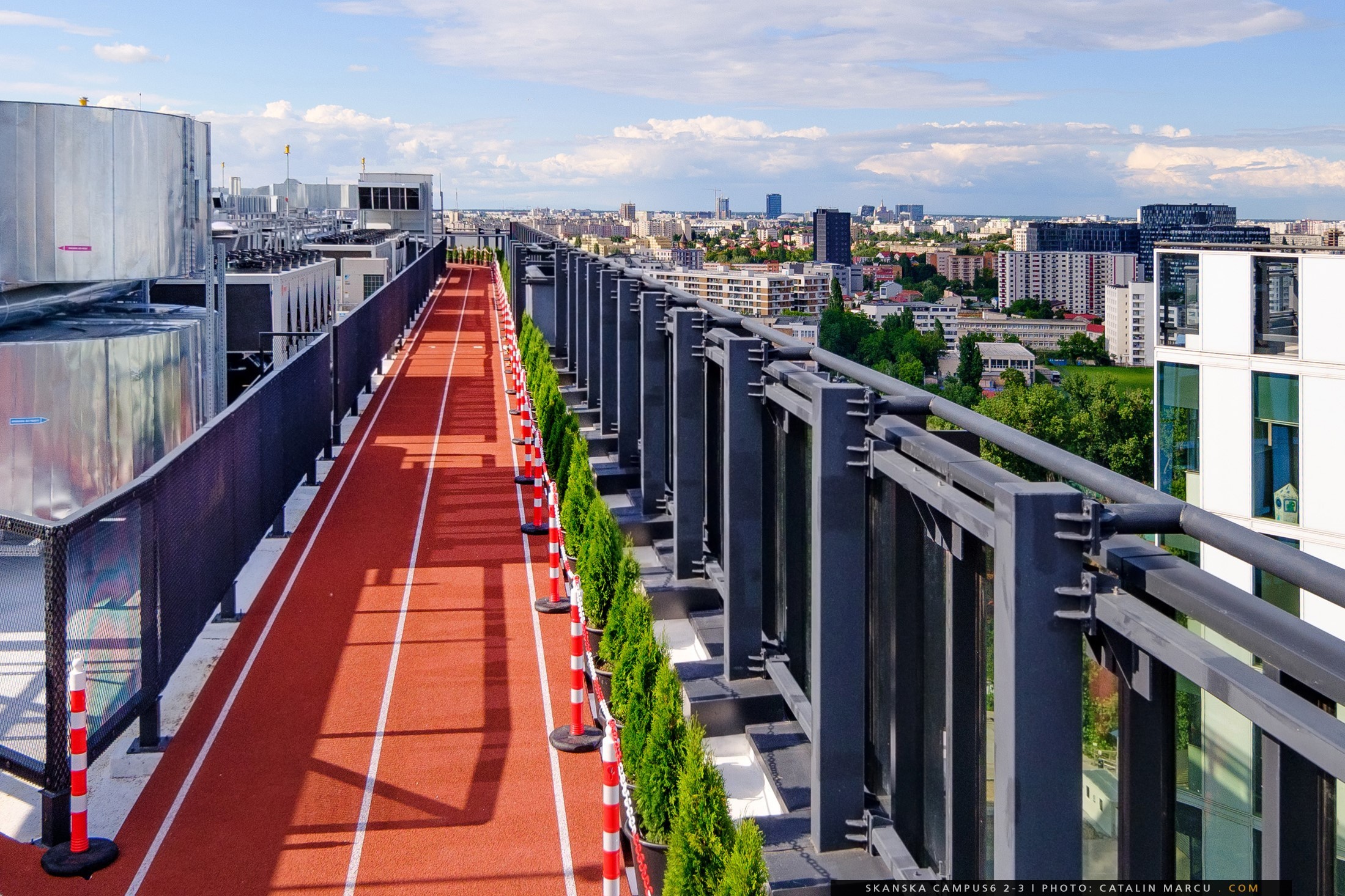 Rooftop jogging track with city skyline views, surrounded by safety barriers and greenery.