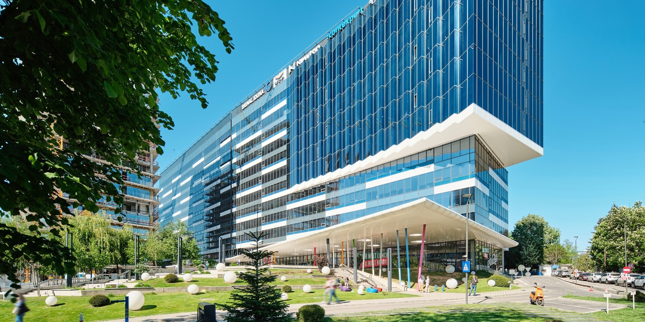 Equilibrium Modern glass-fronted office building with angular design surrounded by greenery and urban landscape.