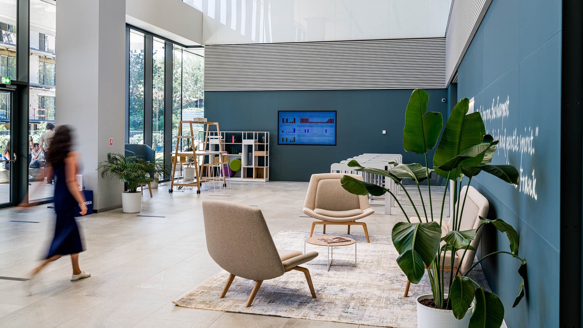 Equilibrium 2 reception Modern lobby with seating, large plants, and a wall-mounted screen, featuring contemporary decor.