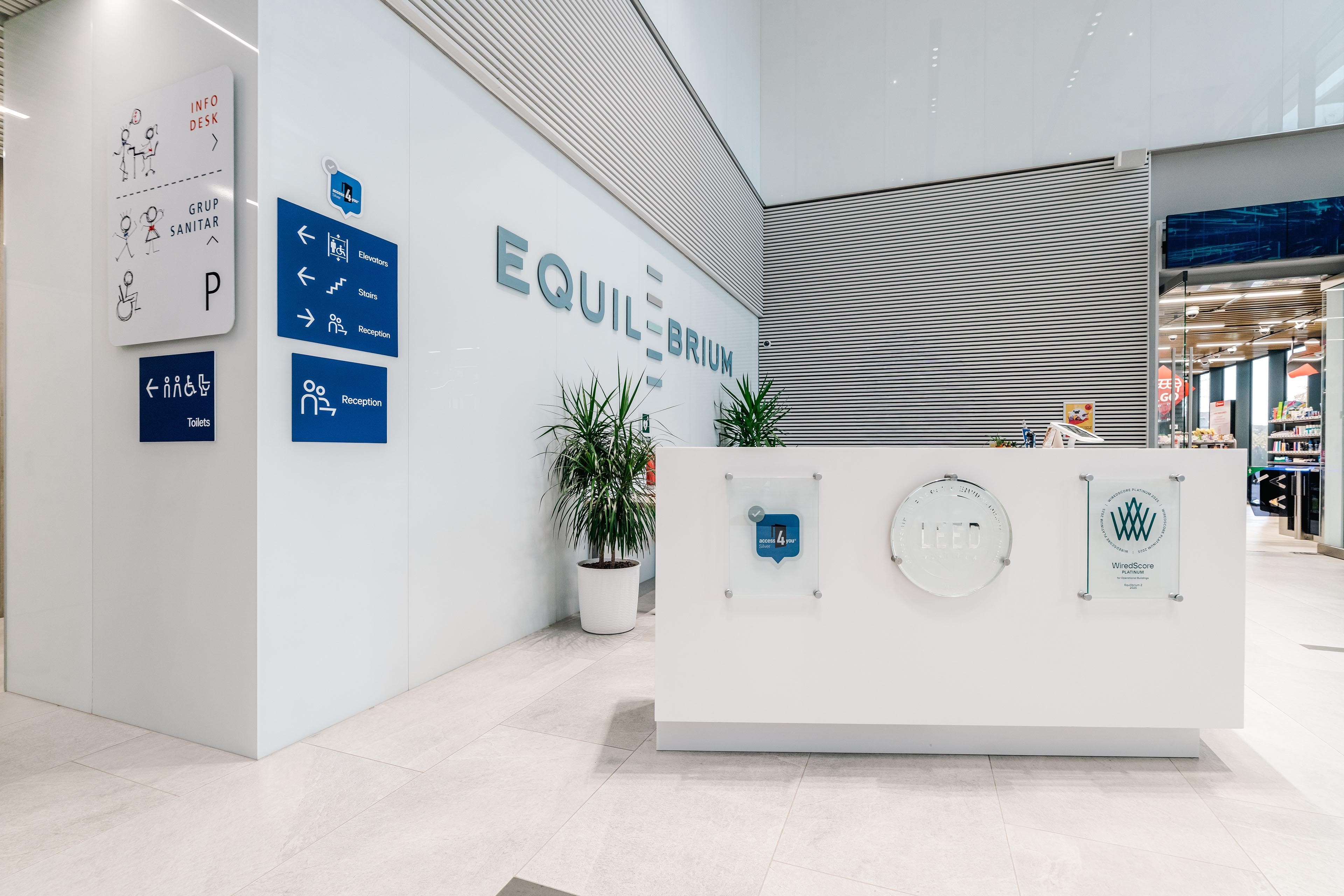Modern reception area with "Equilibrium" signage, directional icons, and potted plants.