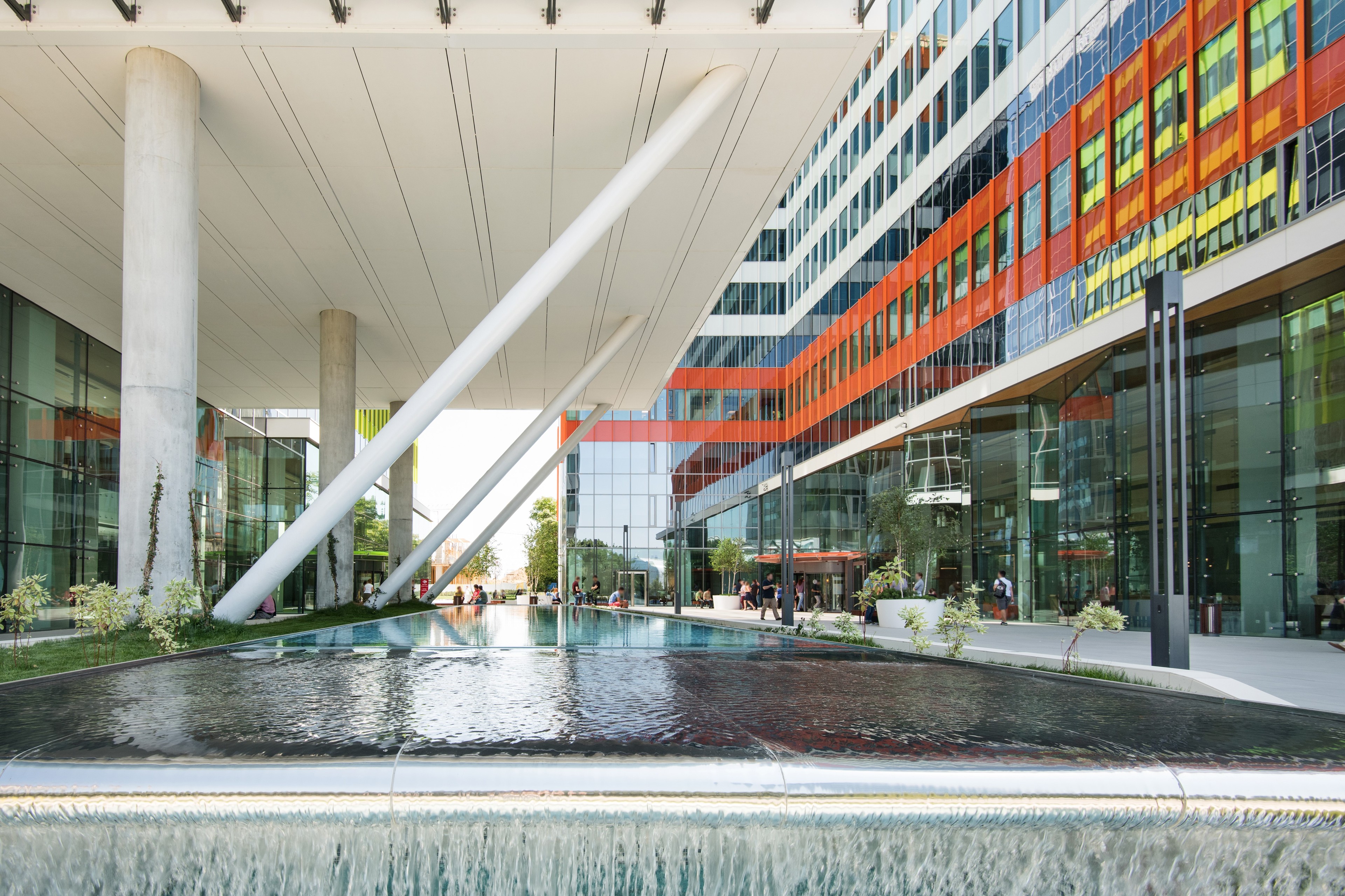 Modern architectural complex with colorful facade and water feature, supported by angled columns.