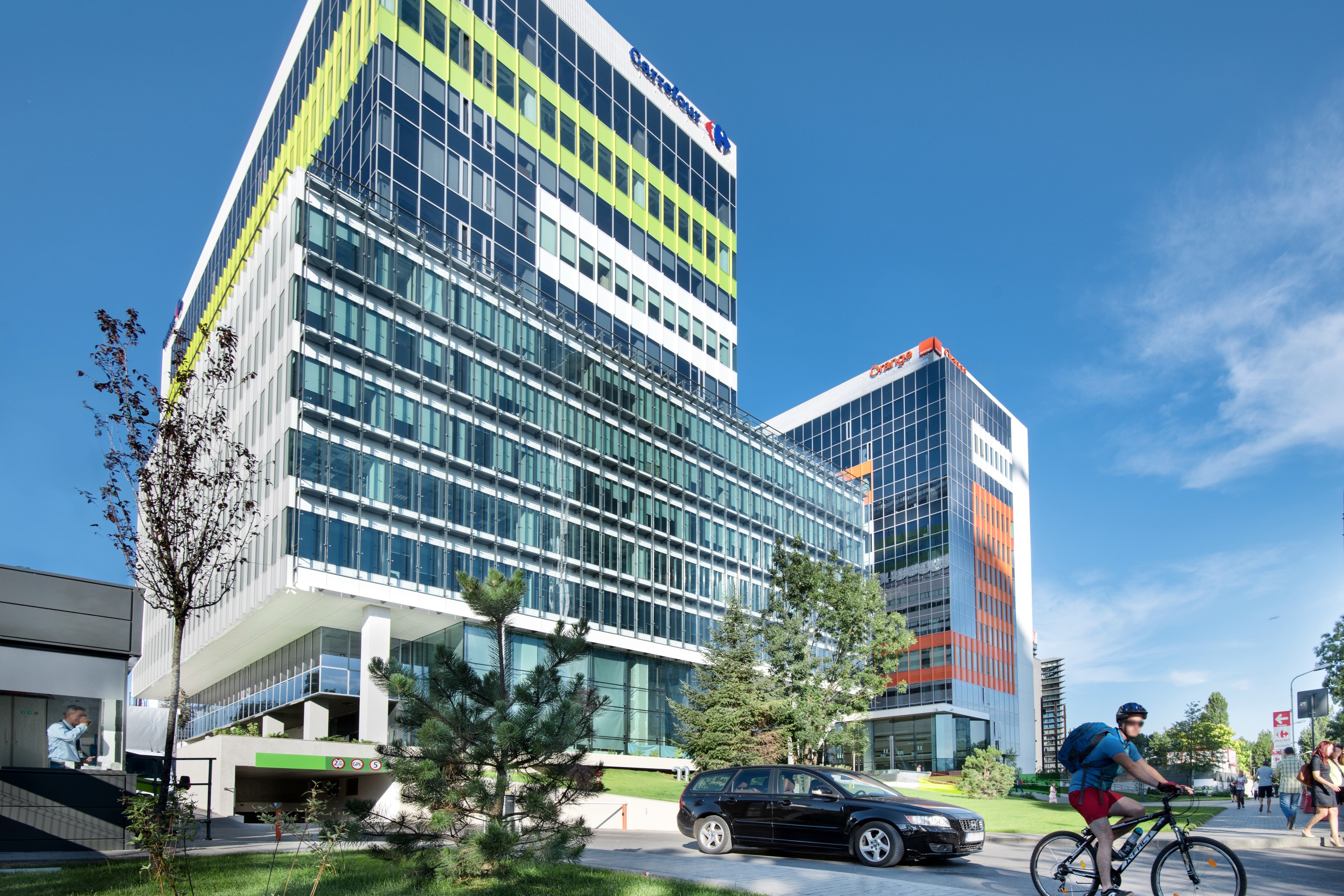 Green Court Bucharest Modern office buildings with glass facades, surrounded by greenery, cyclists, and pedestrians.