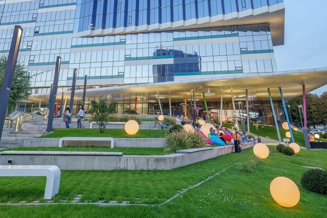 Equilibrium placemaking Modern building with glass facade reflecting a landscaped pond surrounded by greenery and rocks.