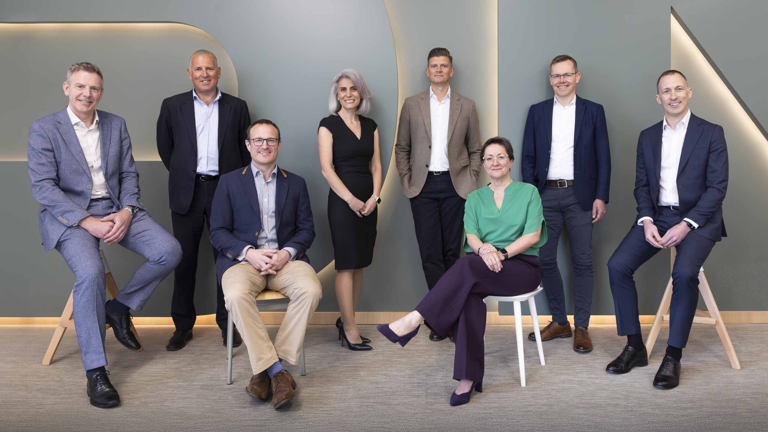 Group of eight professionally dressed business people posing in modern office setting.