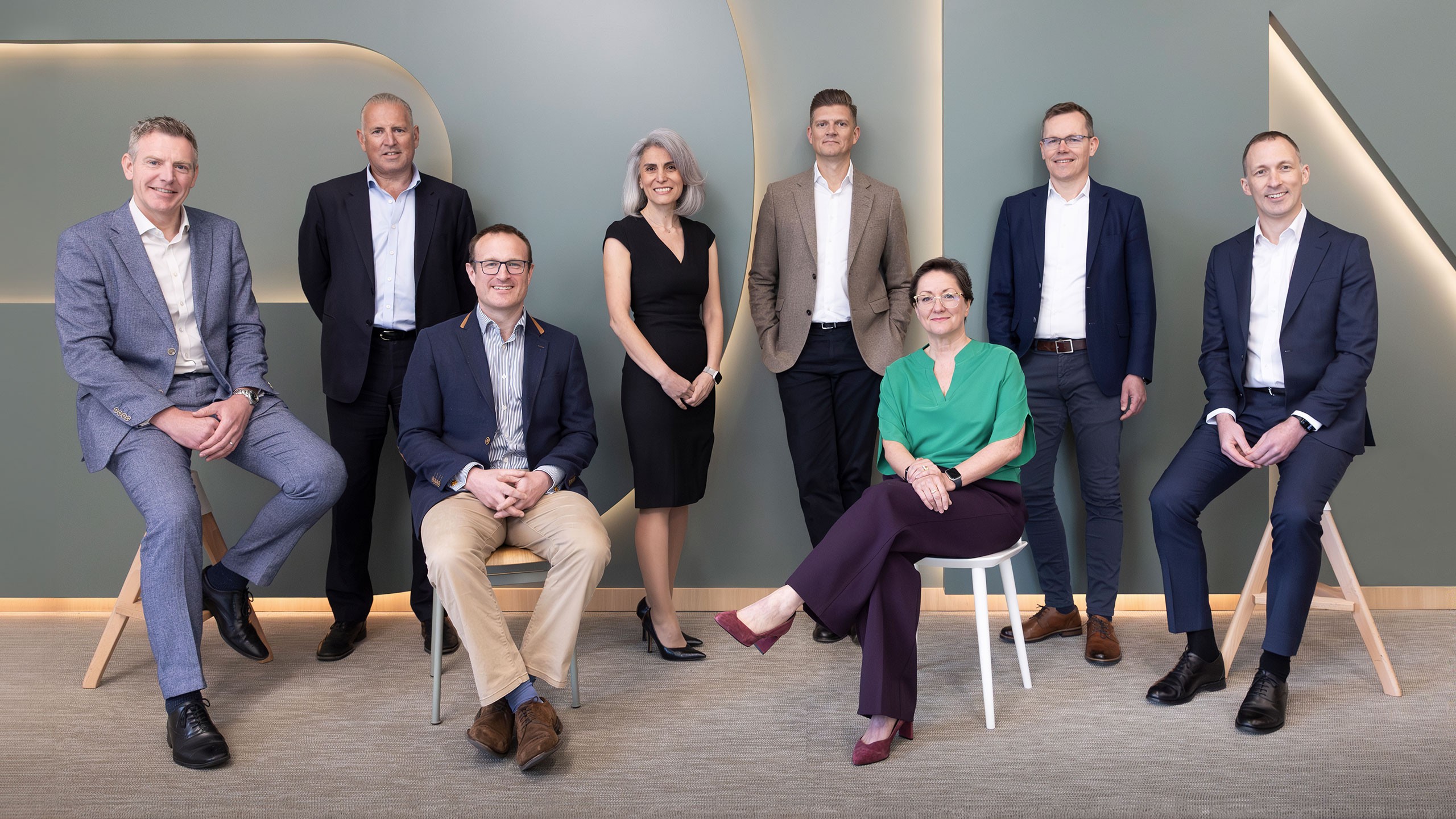 Group of eight professionally dressed business people posing in modern office setting.
