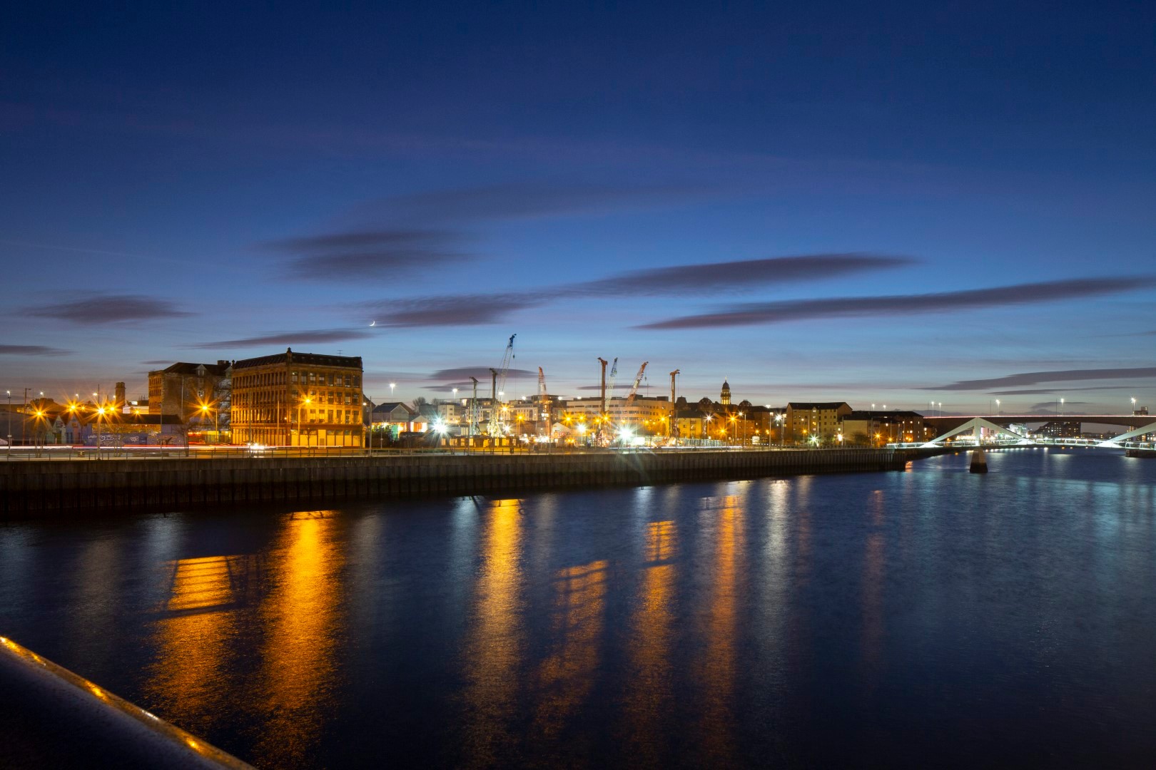 City skyline at dusk with illuminated waterfront reflections Night view of a city waterfront with illuminated buildings and reflections on water.