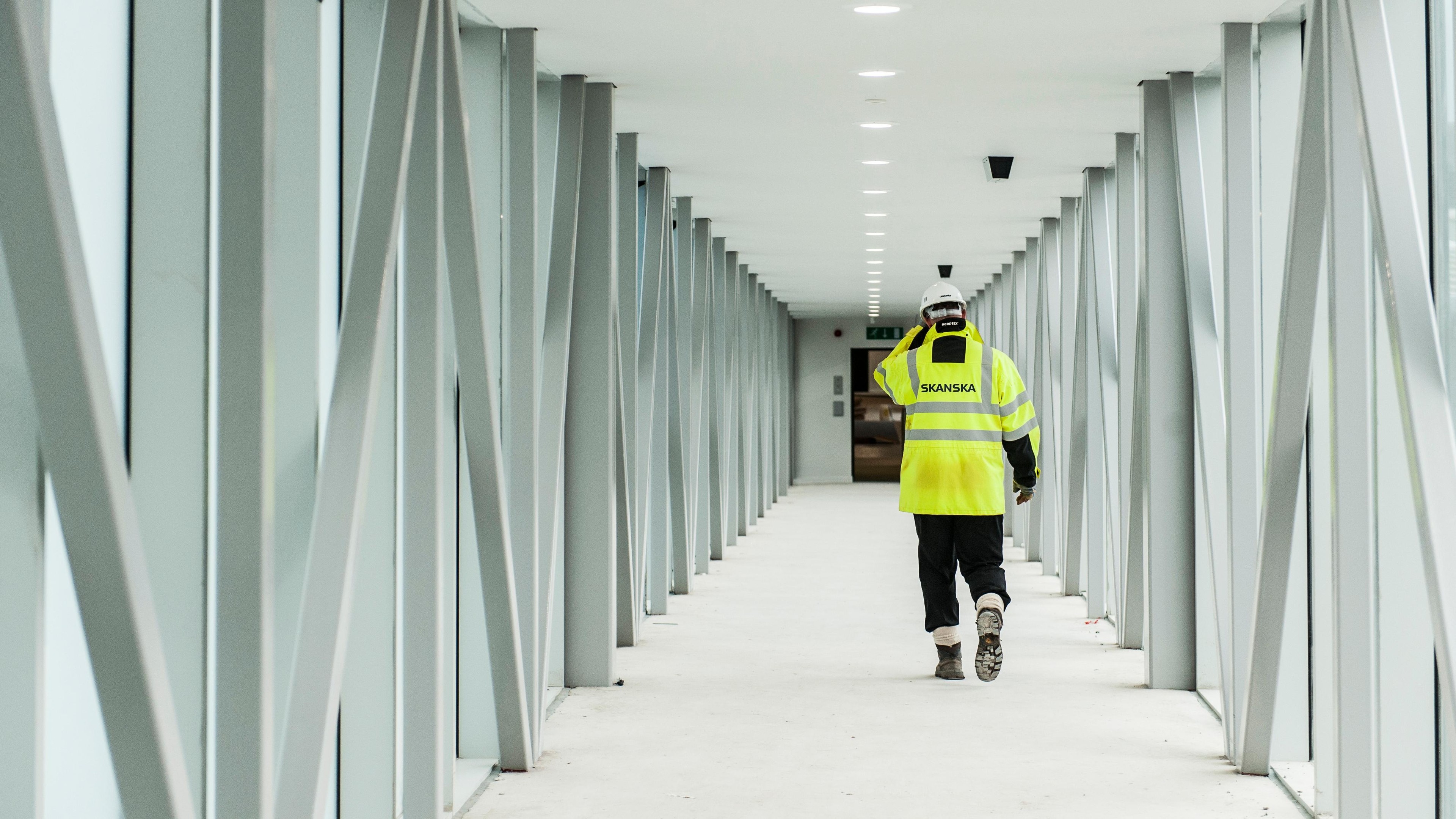 Construction worker walking in modern building corridor Construction worker in high-visibility jacket walking through a modern steel corridor.