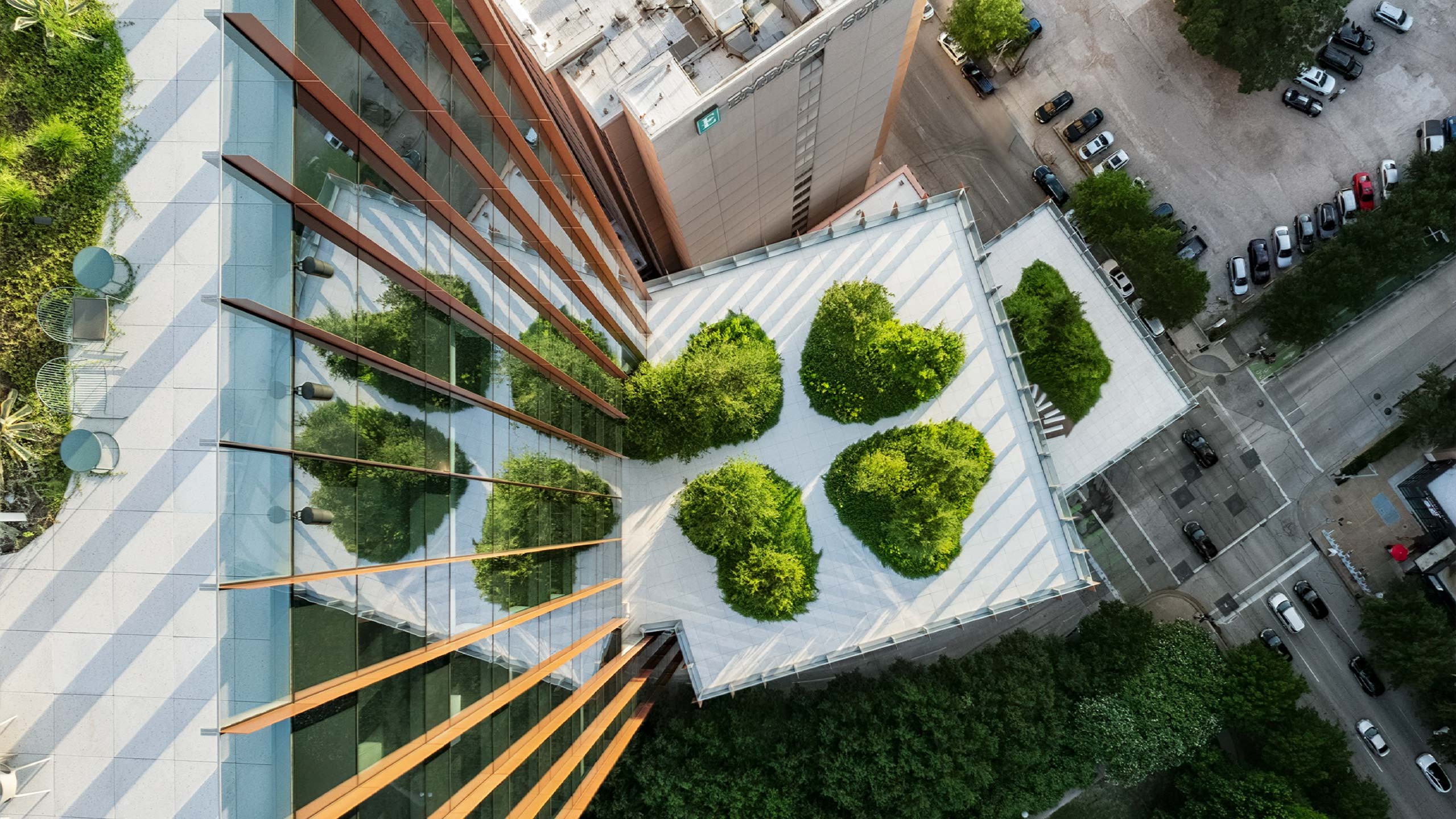Aerial view of a modern building with rooftop gardens and surrounding urban landscape.