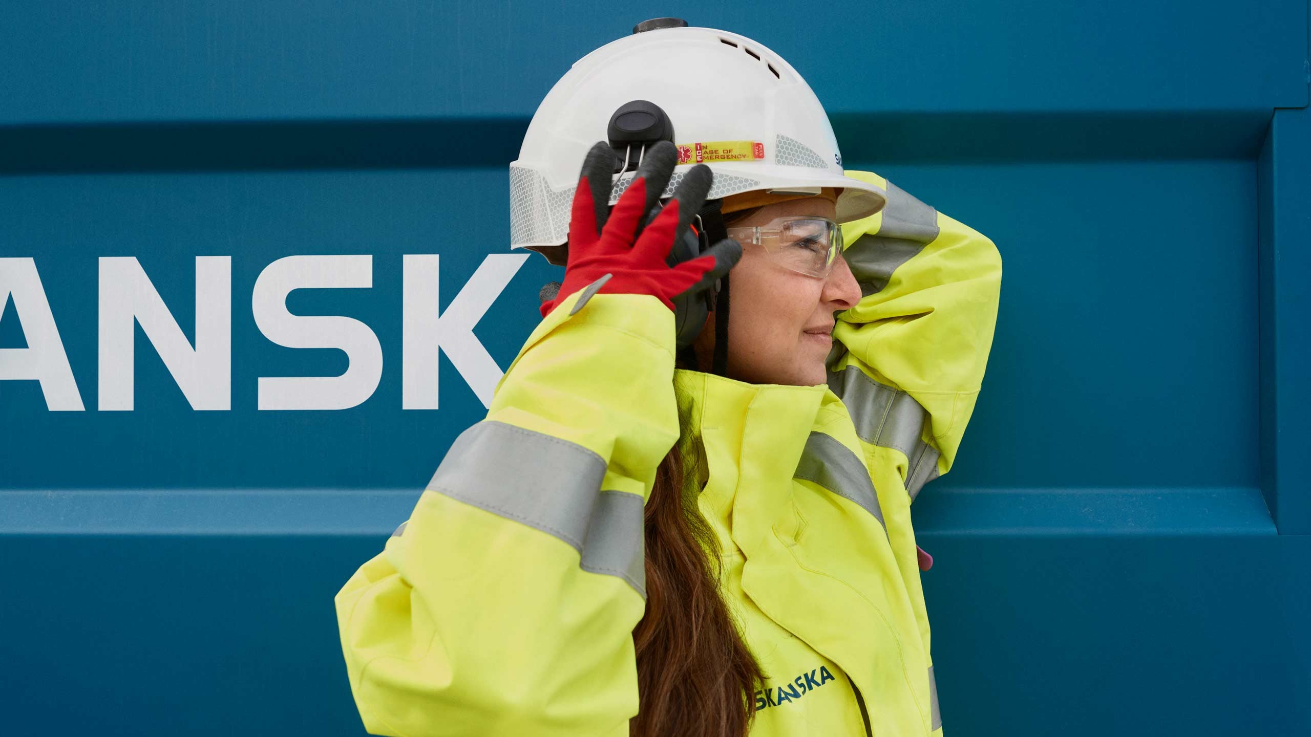 Construction Site Safety: Workers in High-Visibility Gear Construction worker in high-visibility jacket and helmet adjusting safety headphones.