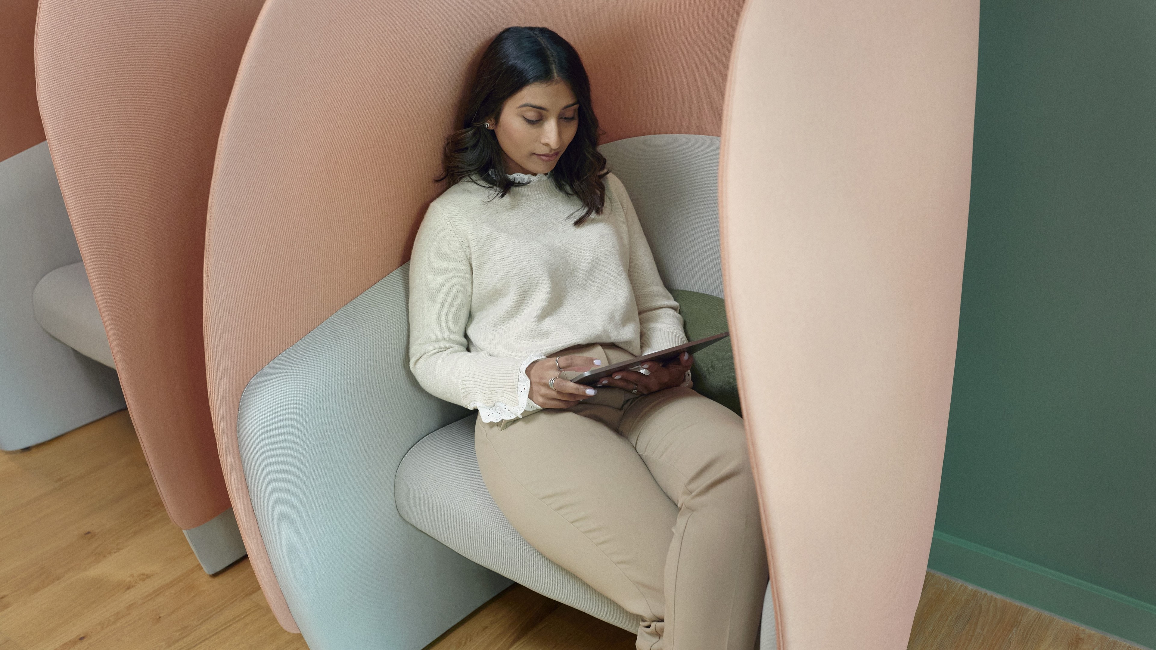 Woman using tablet in modern cozy workspace pod seating Woman sitting in a modern privacy pod chair, using a tablet in a quiet workspace.