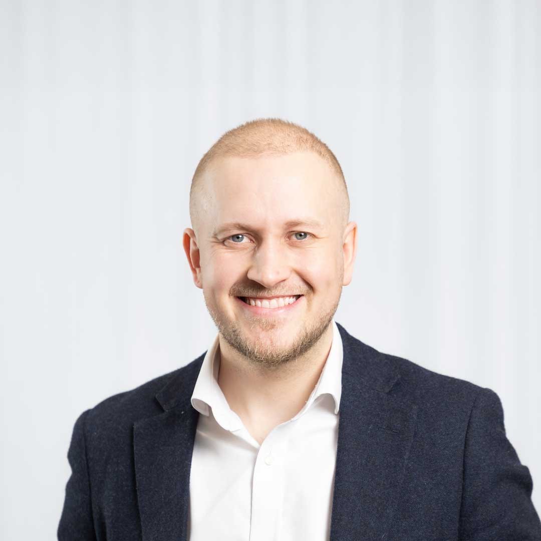 Tom Gould A professional man in a dark suit and white shirt, standing against a neutral background.