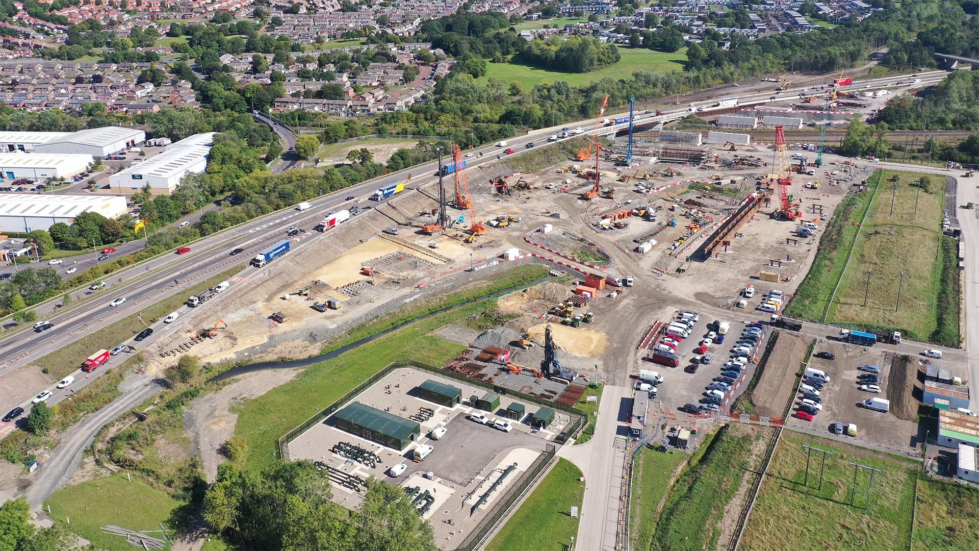 Aerial View of Major Construction Site and Highway Traffic Aerial view of a large construction site with cranes near a busy highway and residential area.