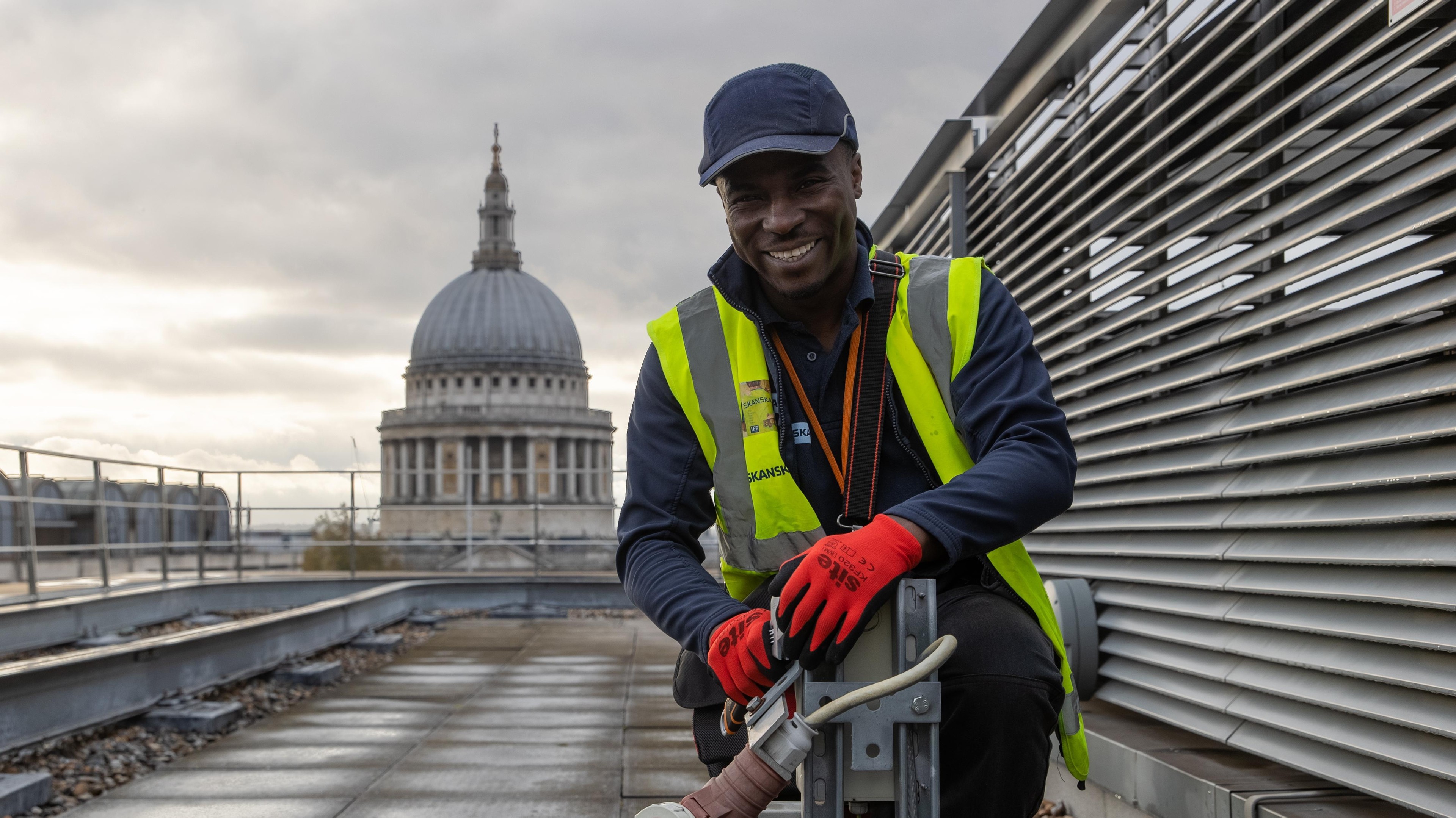 Construction worker in safety gear on rooftop near a historic domed building.