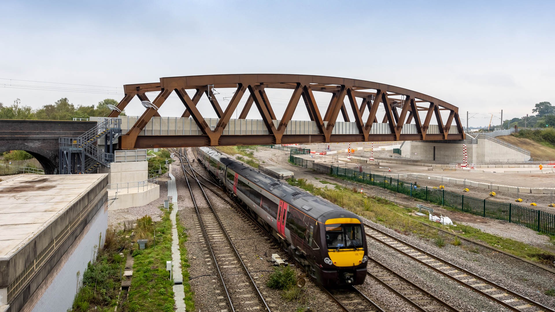 Modern Railway Bridge with Train Passing Underneath Modern passenger train passing under a steel truss bridge on a clear day, showcasing infrastructure.