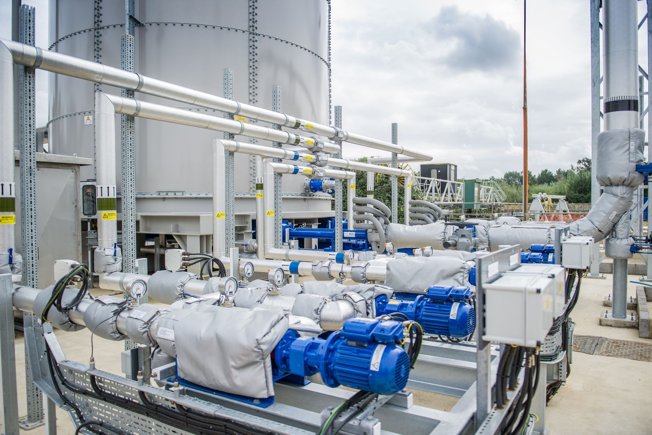 Industrial pumps and pipelines in a modern processing plant Industrial water pumps with blue motors and insulated pipes in an outdoor facility.