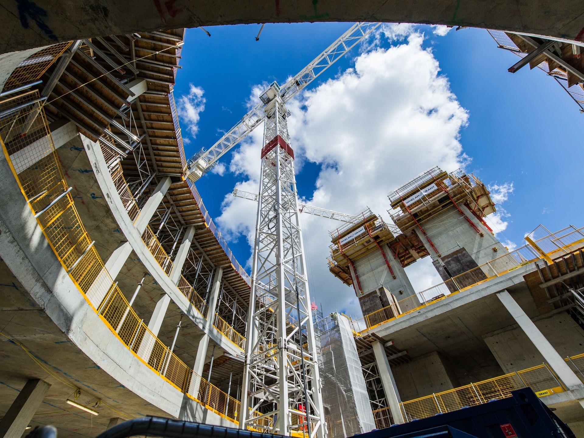 Construction site with tower crane under blue sky and clouds Construction site with a tall crane and concrete building structures under a blue sky.
