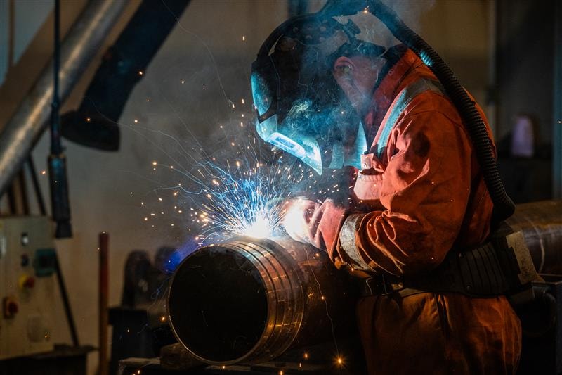 Professional Welder Welding Metal Pipe with Sparks Flying Welder in protective gear welding a metal pipe with sparks flying in an industrial setting.