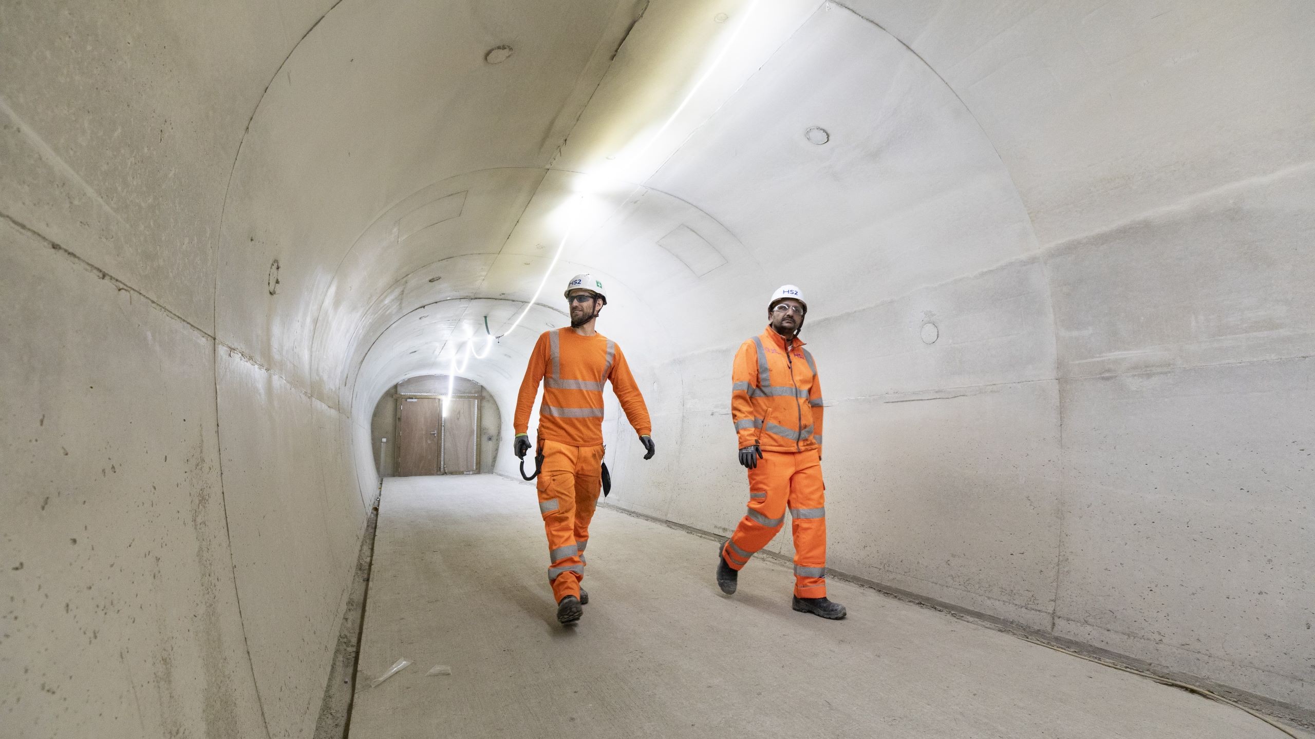 Workers in Orange Safety Gear Walking in Concrete Tunnel Cross passages, HS2 in London