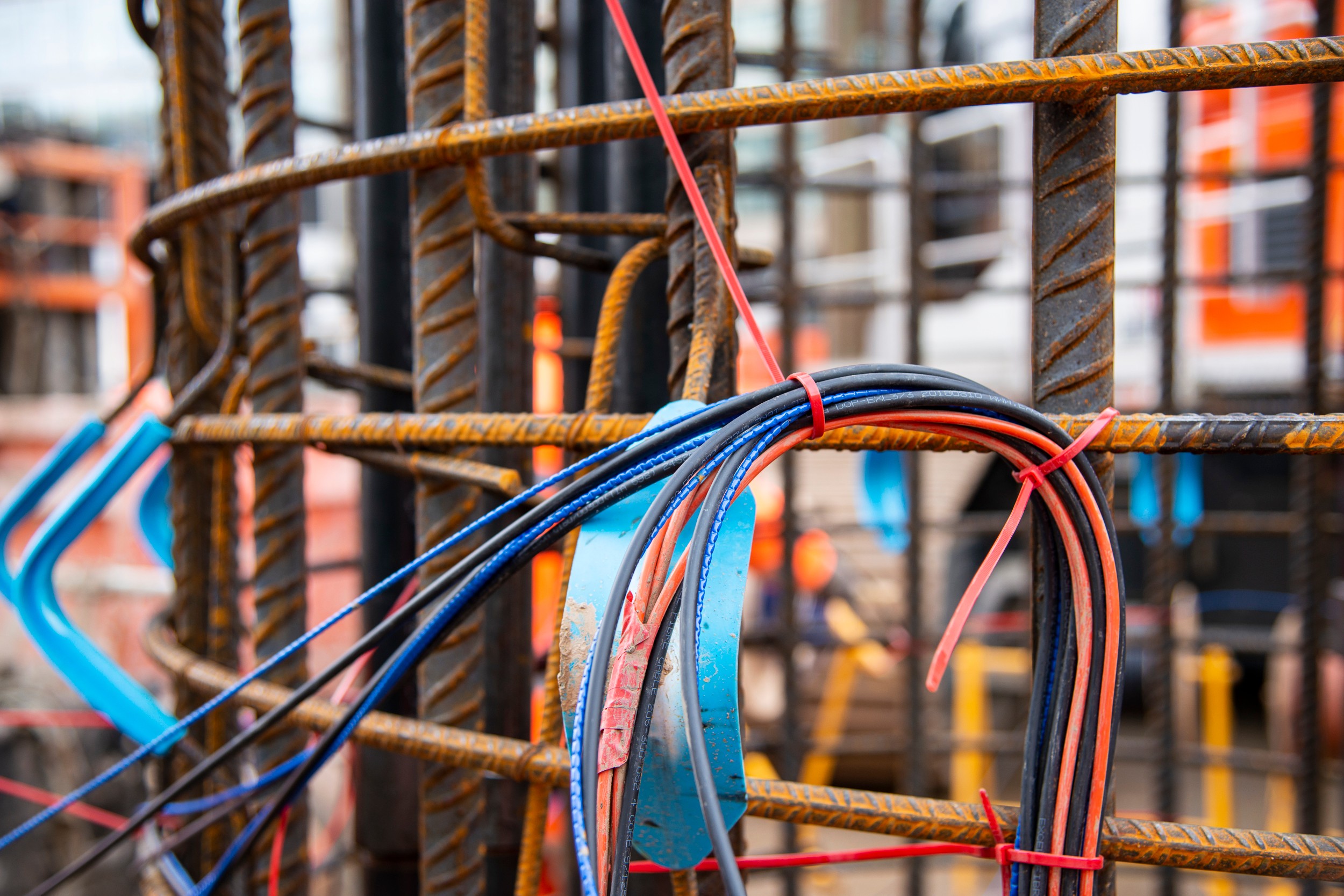 Colorful electrical wires tied on rusty steel rebar at construction site Blue and red electrical wires tied to rusty steel rebar at a construction site.
