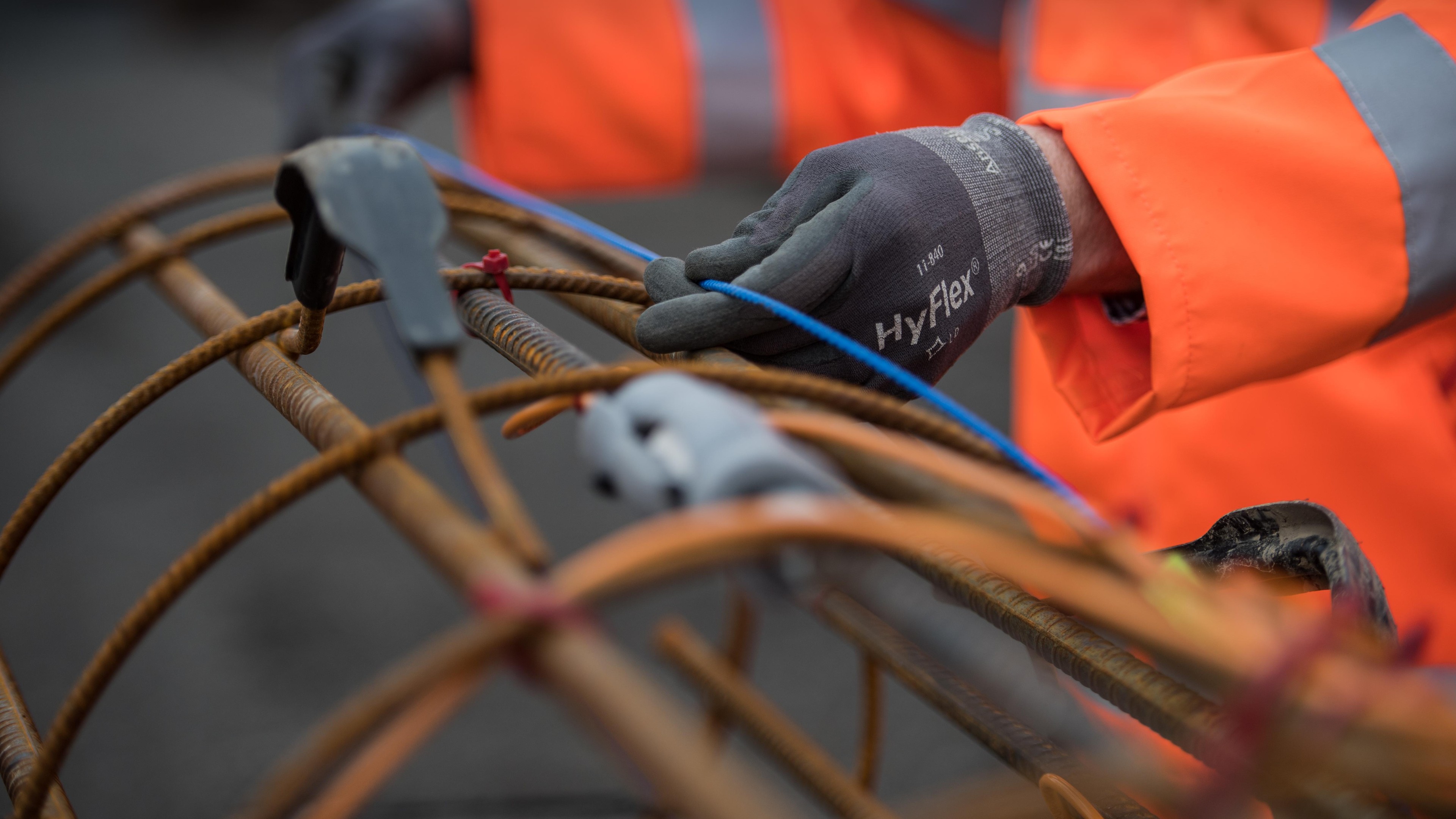 Worker tying steel rebar with wire for construction safety Construction worker wearing gloves ties blue wire around rusted steel rebar on site.