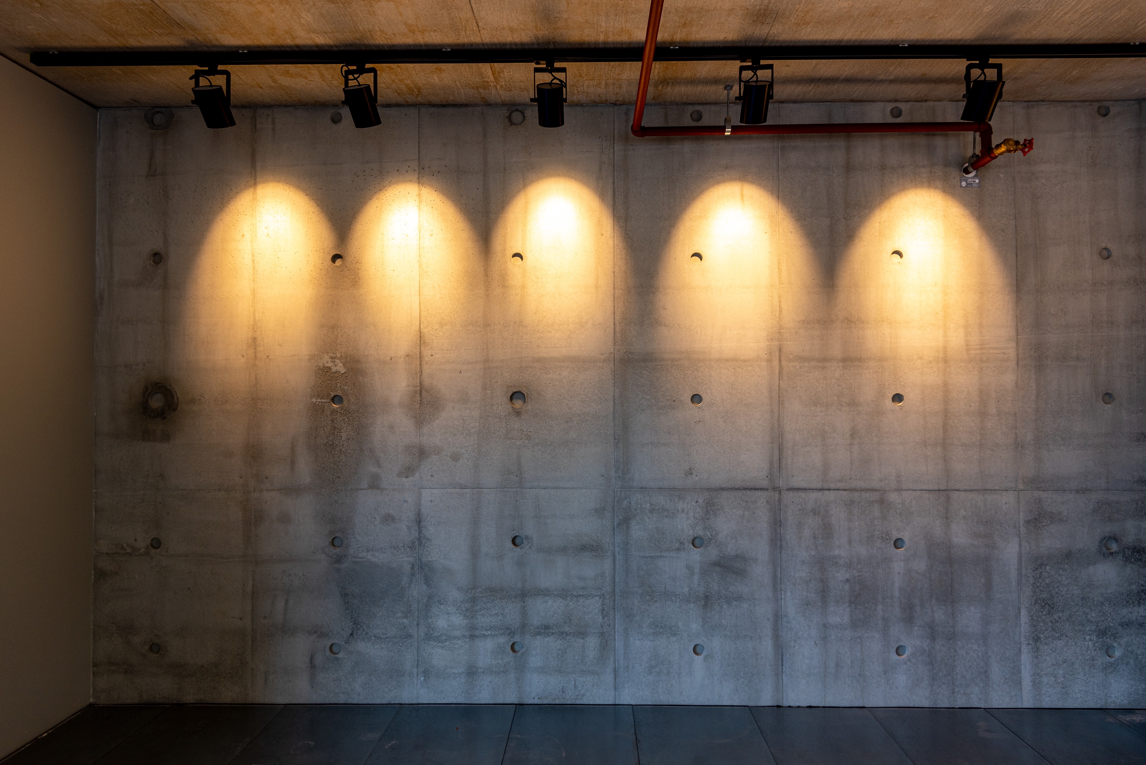 Concrete wall illuminated by five warm spotlights in an industrial-style room.