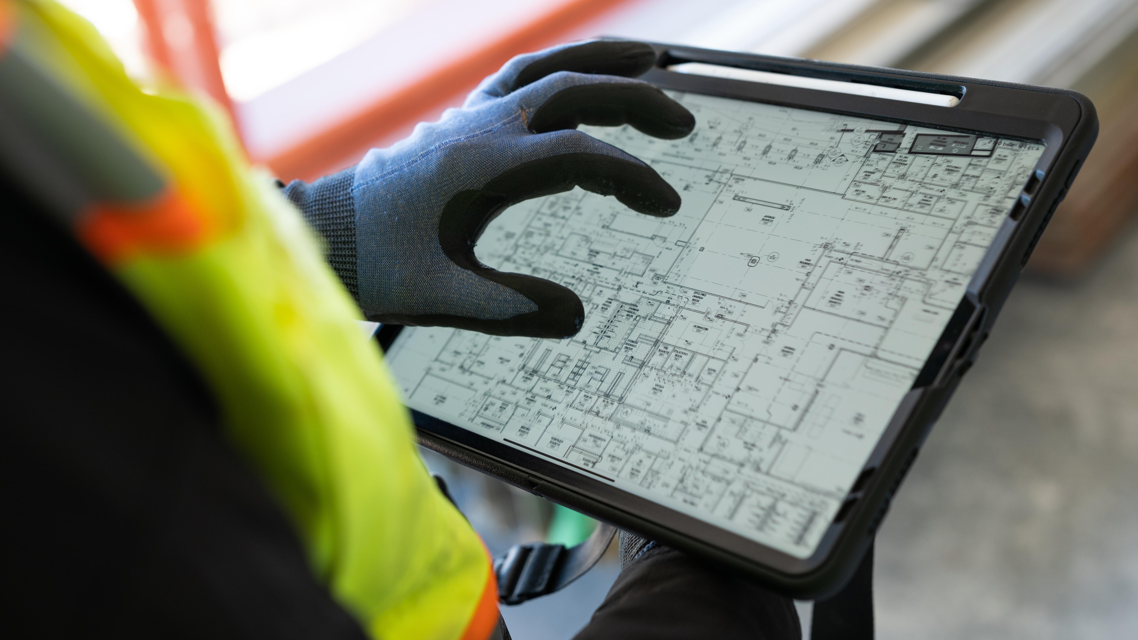 Construction worker in safety gear reviewing building plans on a digital tablet.