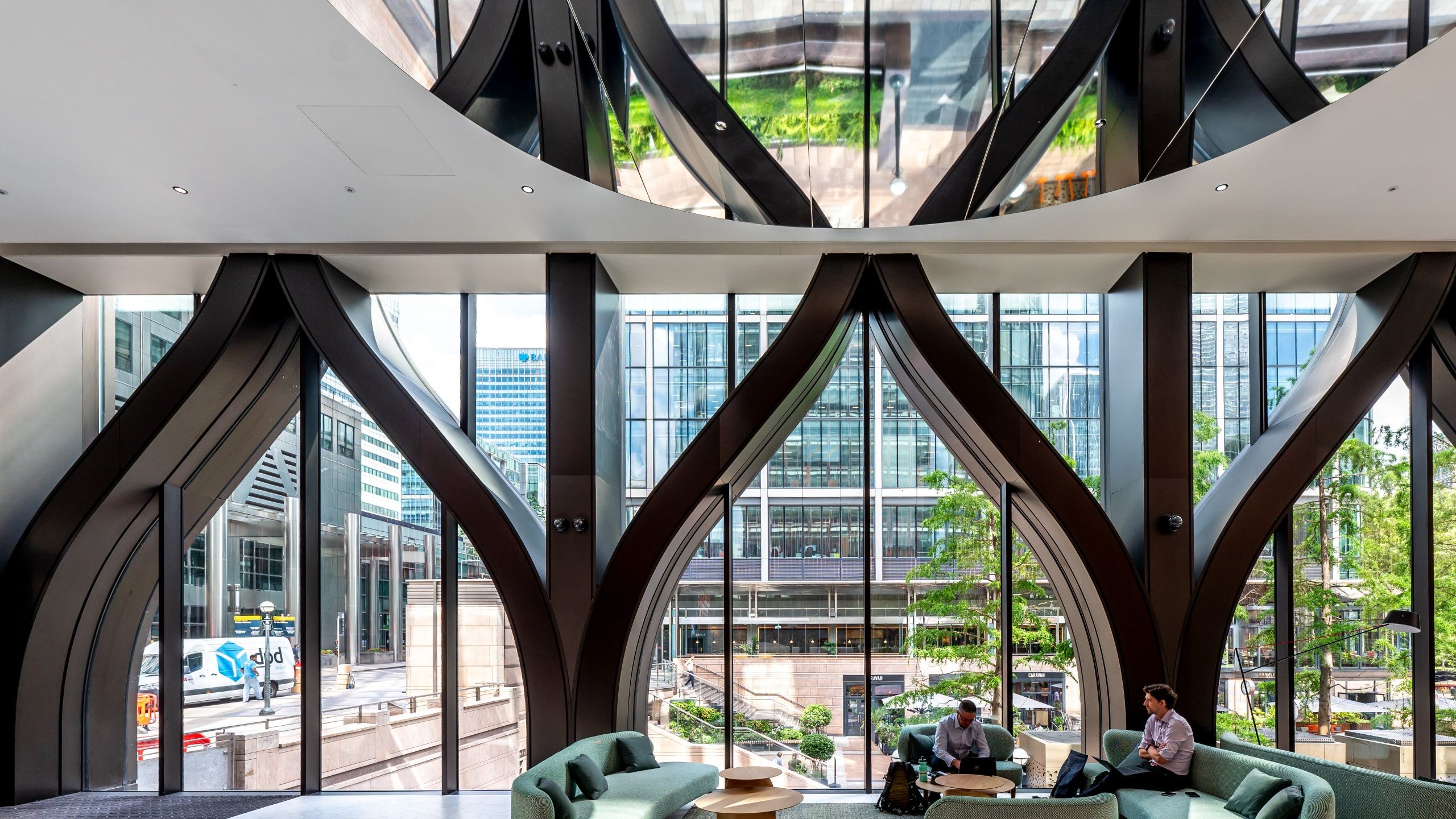 Modern office lounge with large arched windows and green sofas overlooking cityscape.