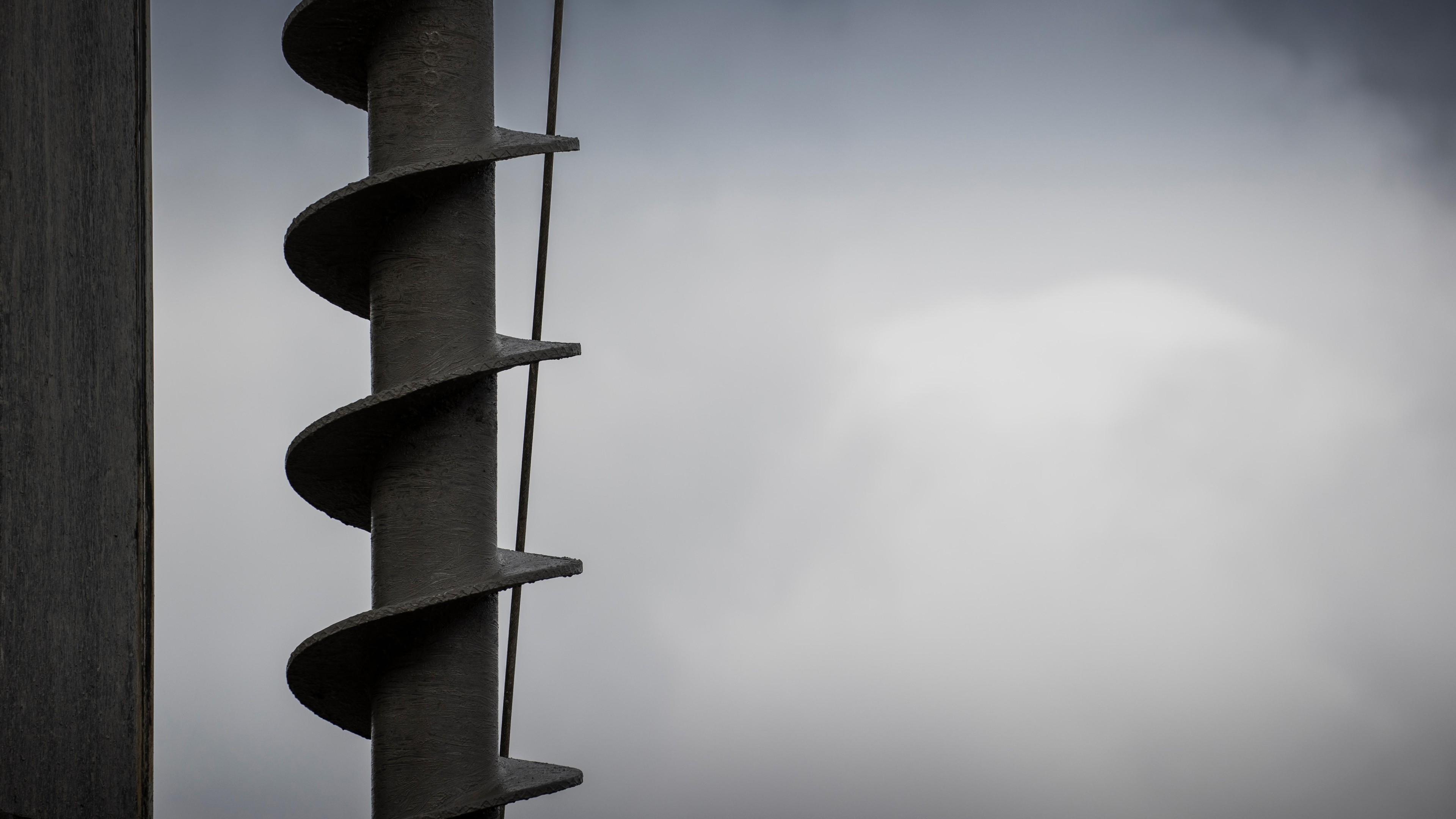 Close-up of Industrial Metal Spiral Drill Bit with Gray Background Close-up of a metal spiral drill bit against a gray cloudy sky background.